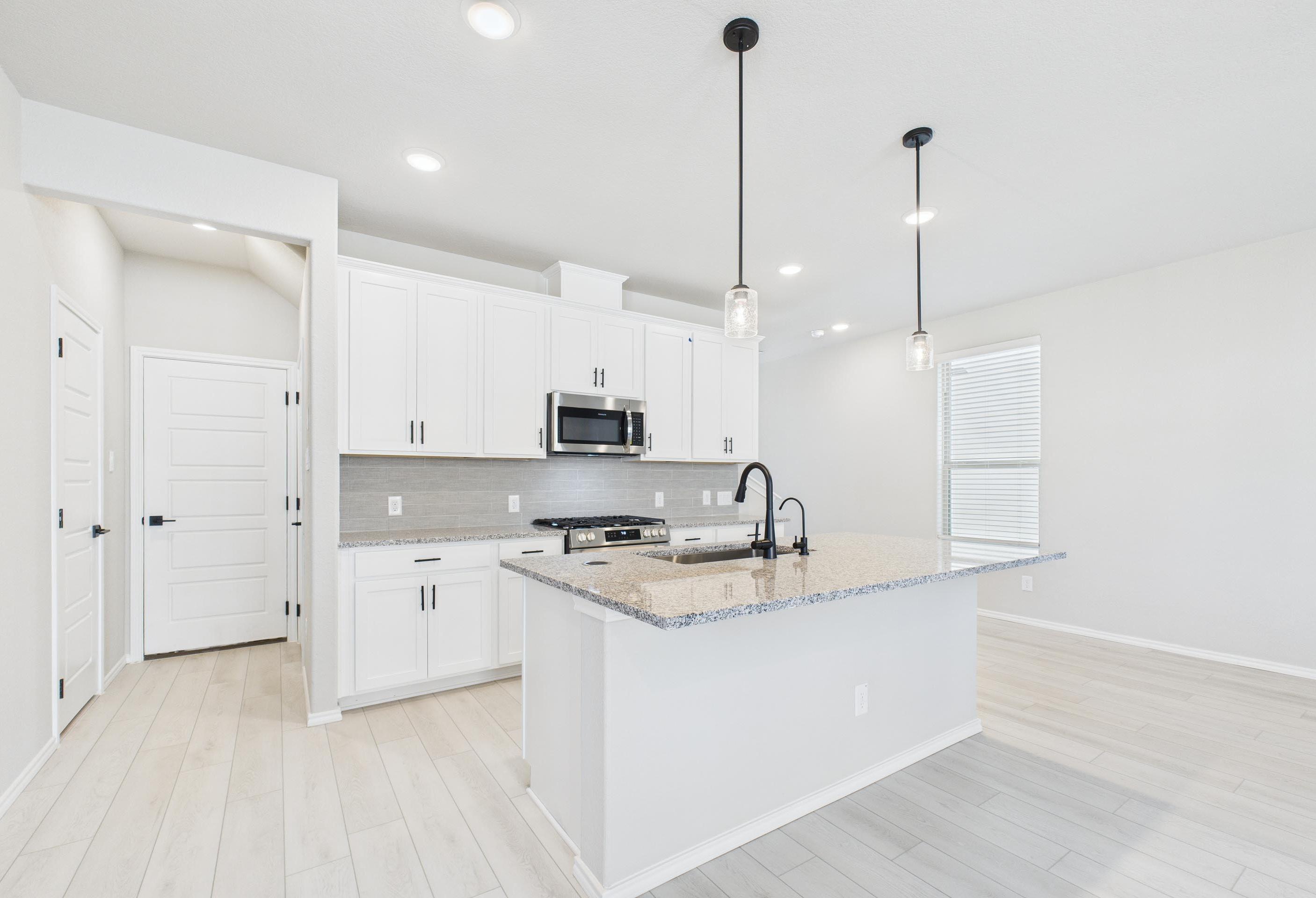 Modern kitchen in The Charlotte A featuring white cabinets, granite island, and pendant lighting in San Antonio, Texas.