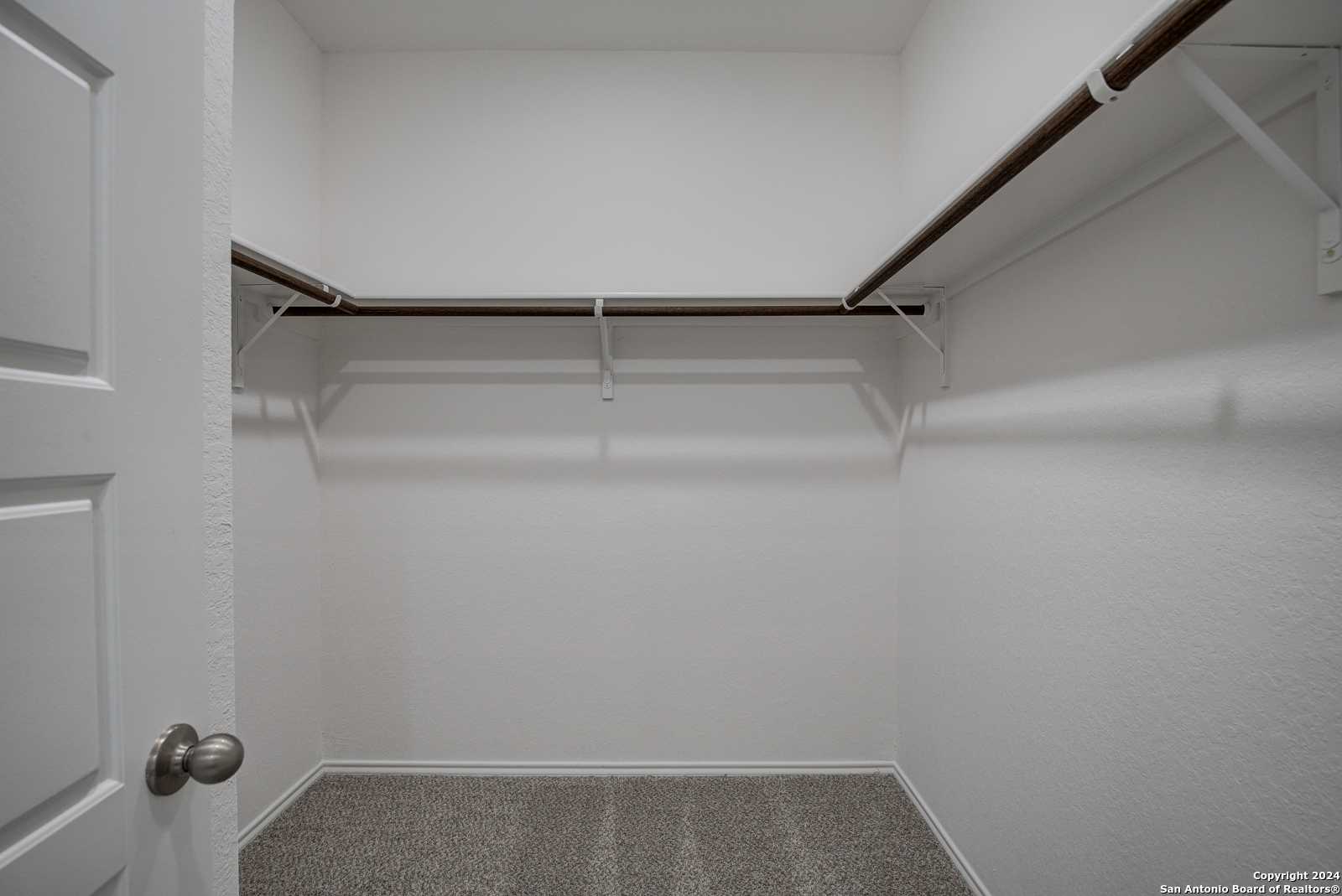 Spacious empty walk-in closet with wooden hanging rods and carpet floor in master suite of Davidson Homes The Douglas D, Seguin, Texas