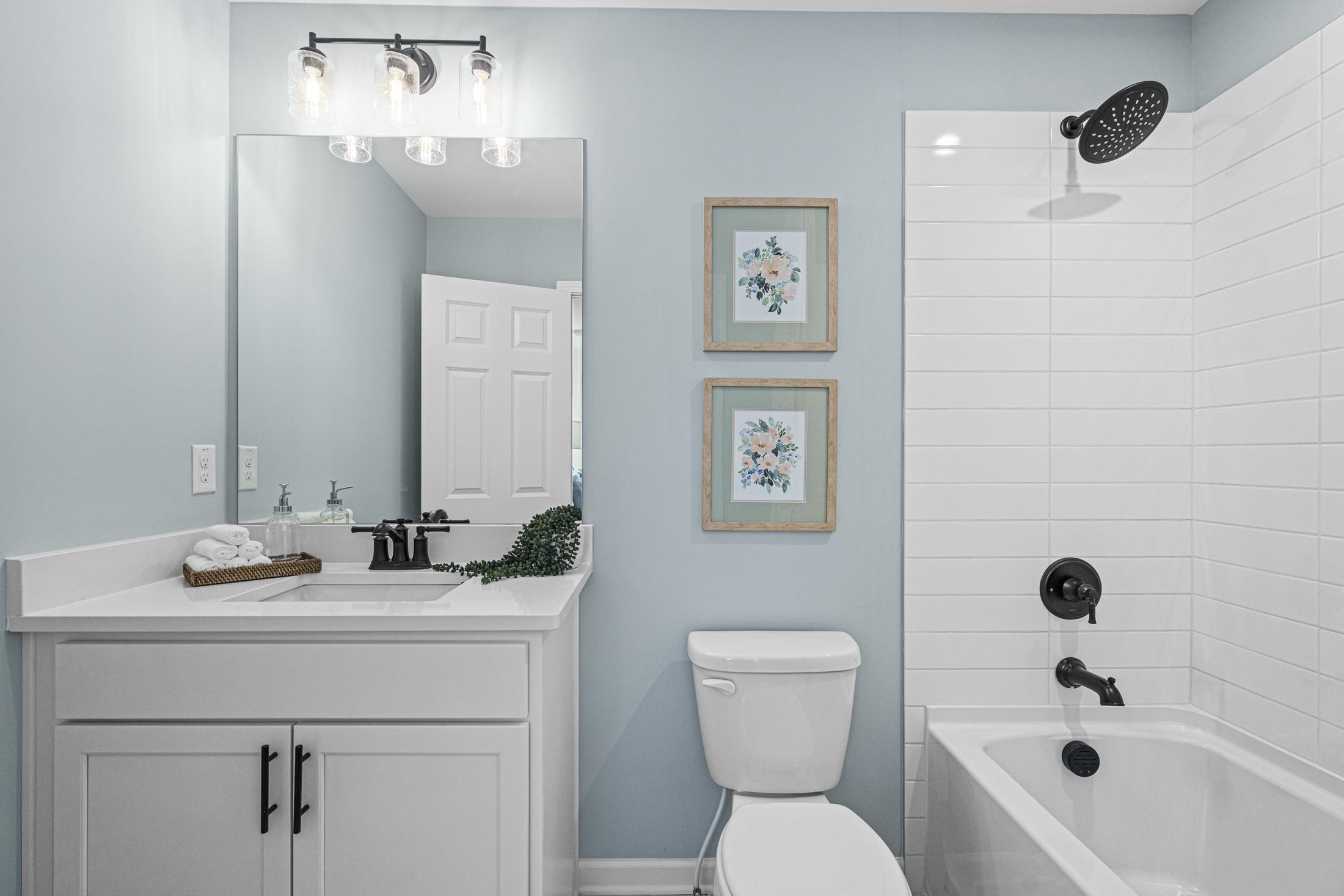 Modern master bathroom in The Hickory B with white double vanity, soaking tub, rainfall shower, blue walls, and floral art