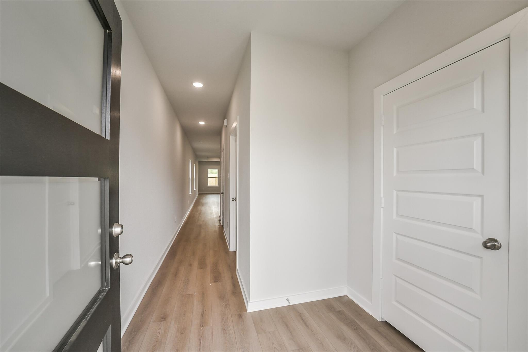 Bright hallway with luxury vinyl plank floors, white walls, and paneled doors in Davidson Homes The Frio F, Conroe, Texas