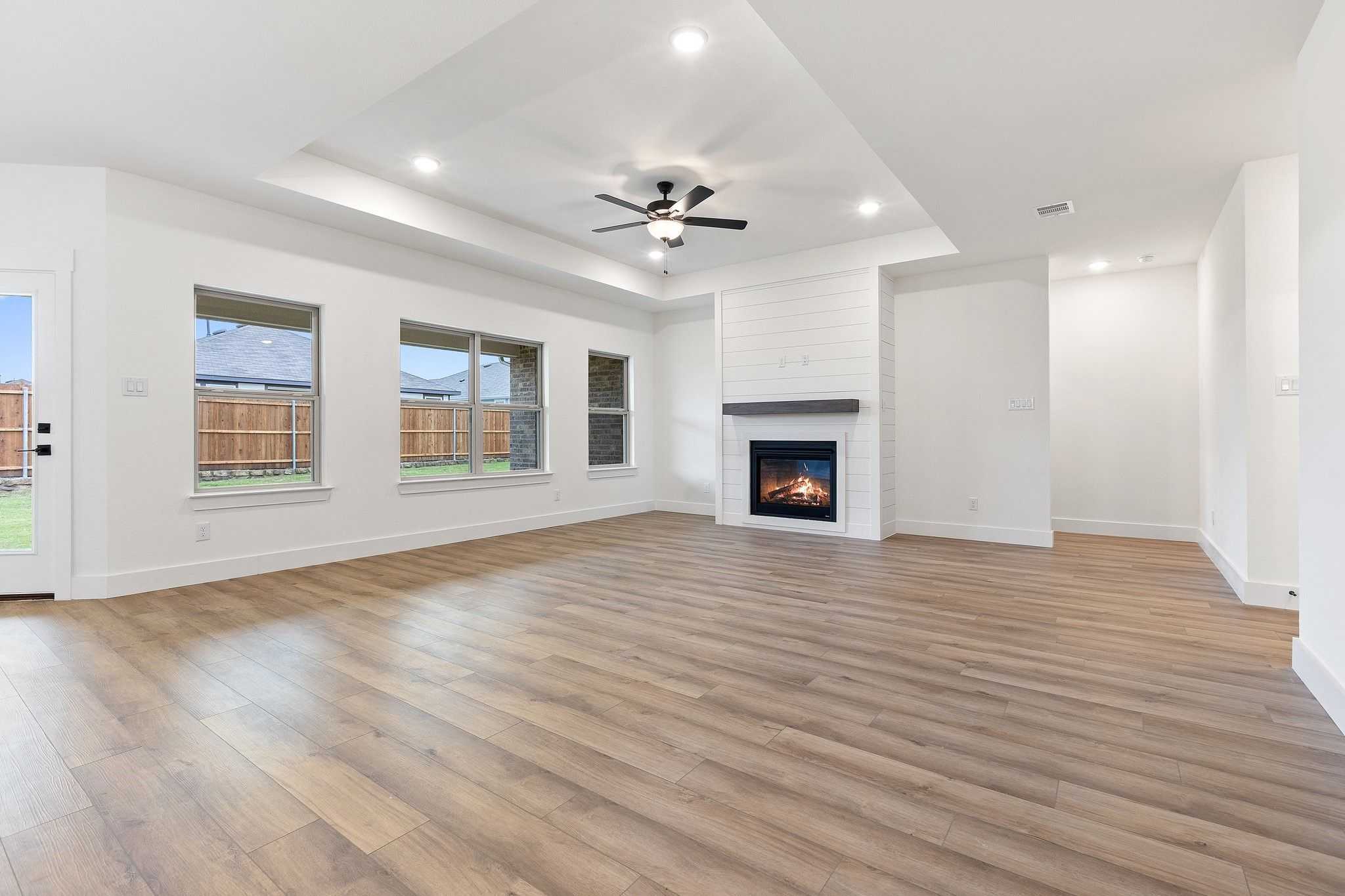 Spacious living room with white brick gas fireplace, hardwood floors, and large windows in Davidson Homes The Rockford C, Josephine, TX