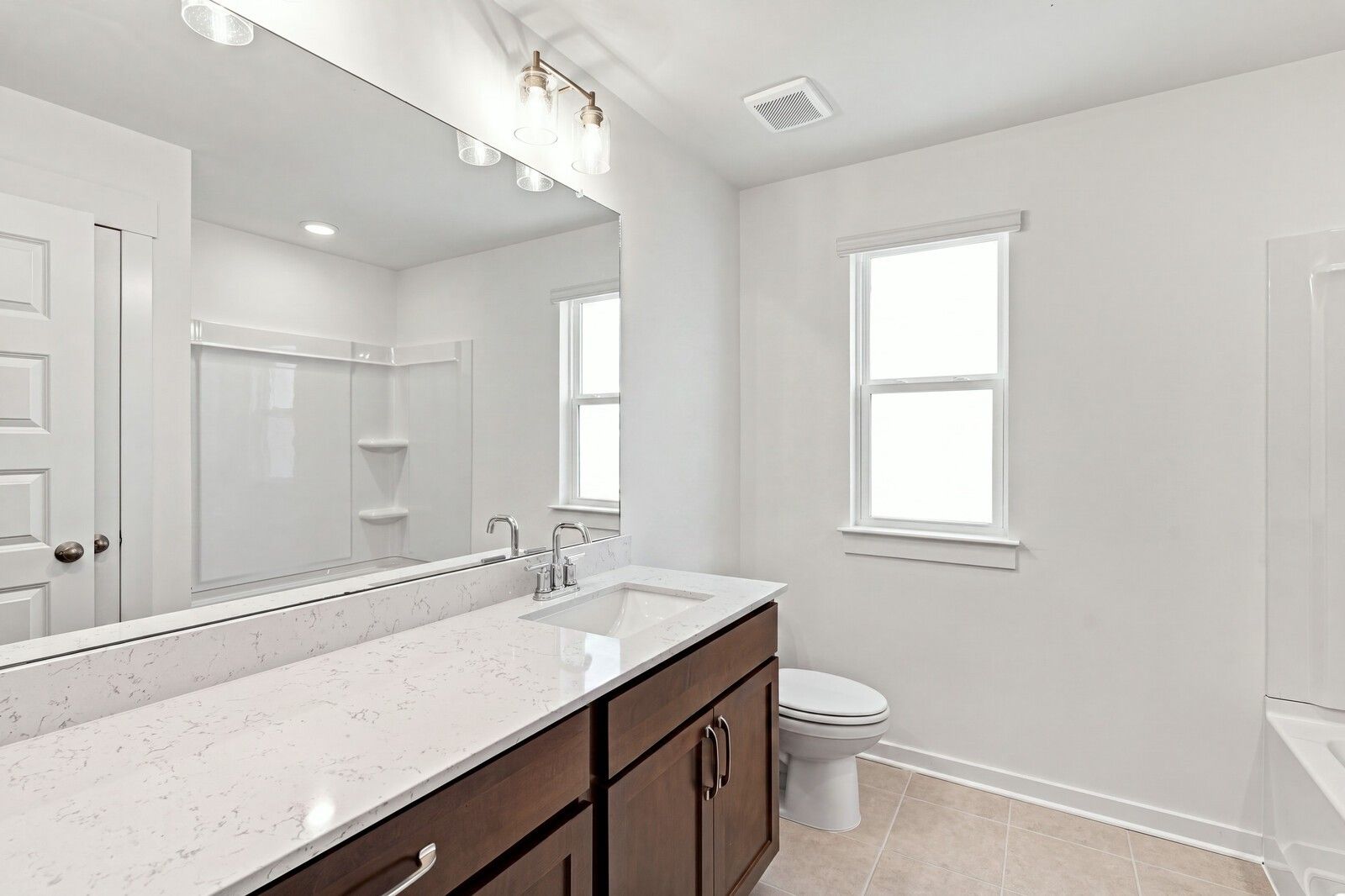 Bathroom with quartz vanity countertop, dark wood cabinets, and large mirror in Davidson Homes Willow C plan, Gallatin TN