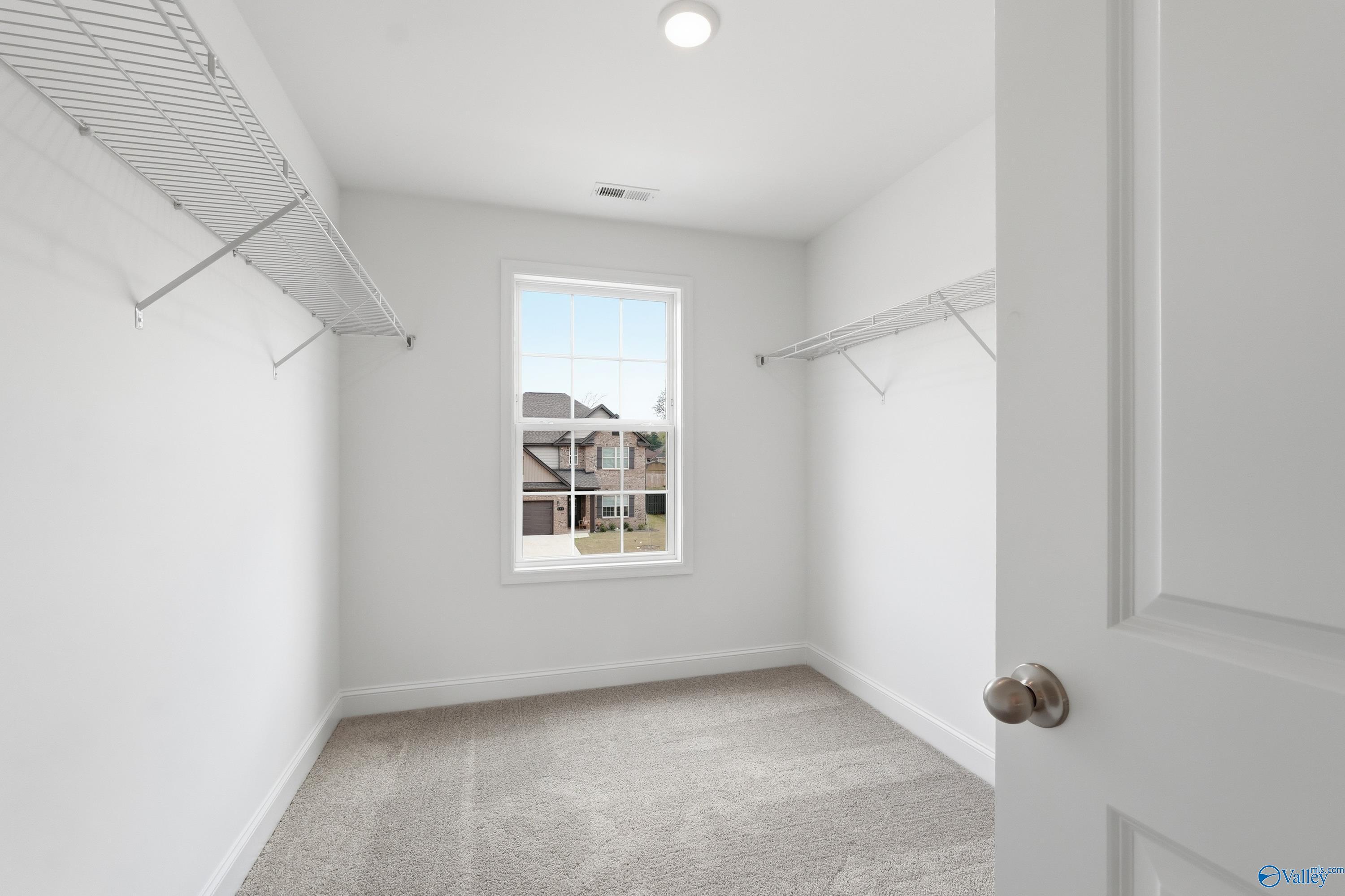 Spacious walk-in closet with wire shelving, hanging rods, and window view in Davidson Homes The Shelby B, New Market, Alabama