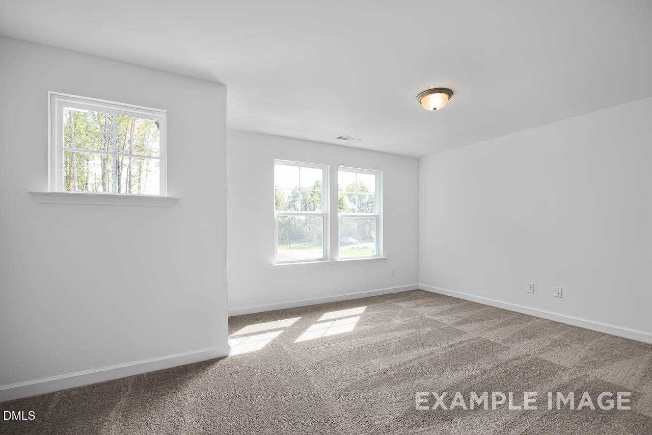 Bright empty bedroom with double windows, natural light, white walls, and beige carpet in The Willow D, Zebulon, NC
