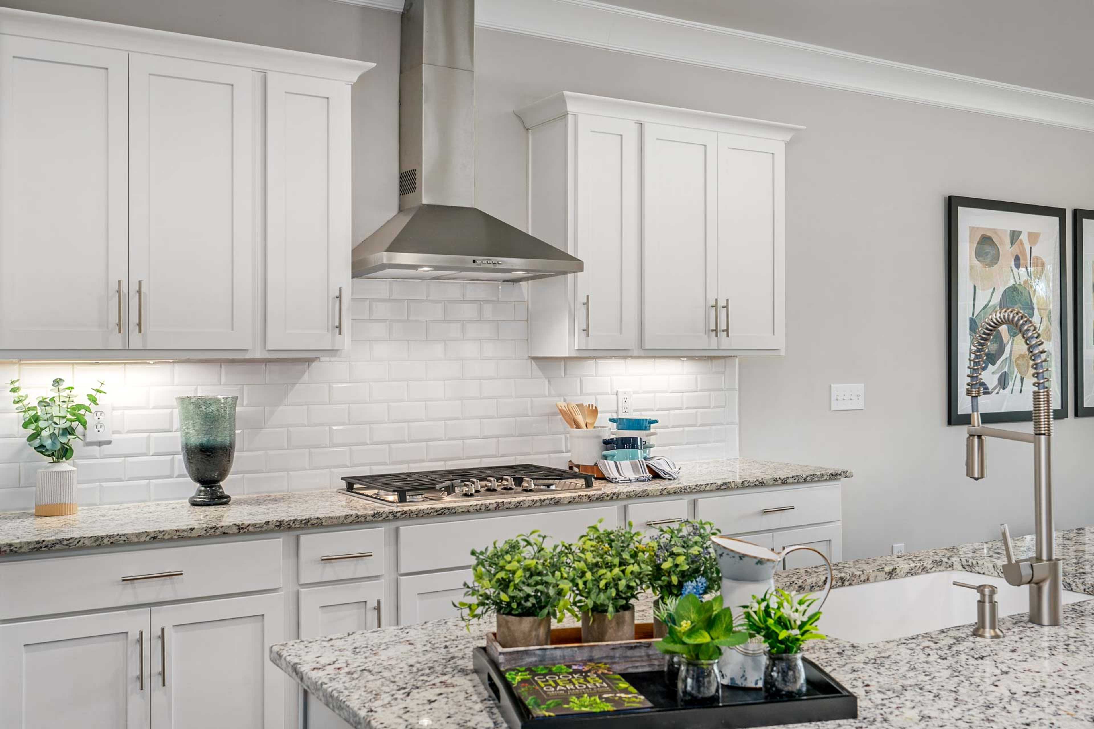 Modern kitchen in Kendall Downs Toney AL with white shaker cabinets, granite island, stainless steel appliances, subway tile backsplash, potted plants