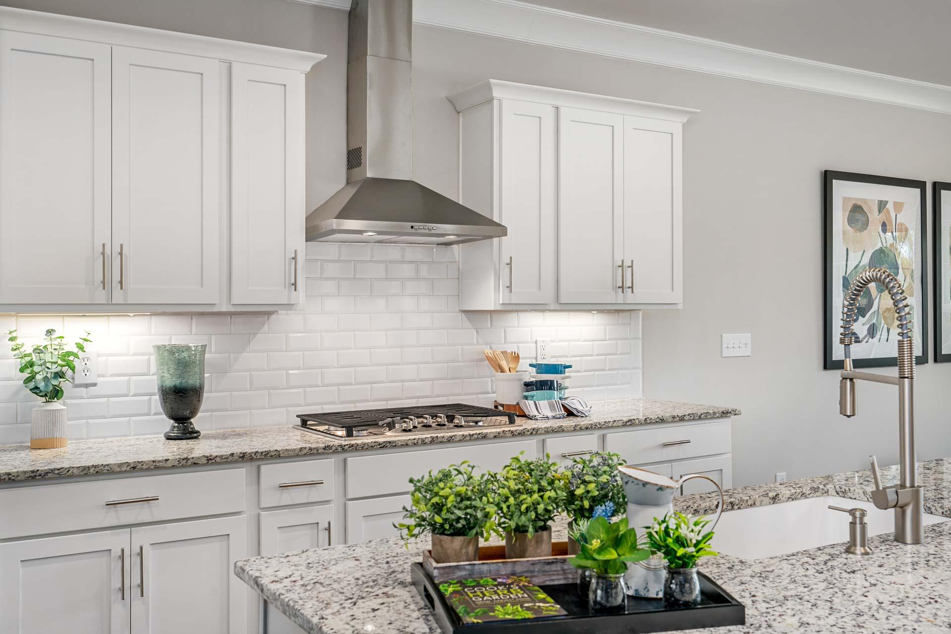 Modern kitchen in Kendall Downs Toney AL with white shaker cabinets, granite island, stainless steel appliances, subway tile backsplash, potted plants