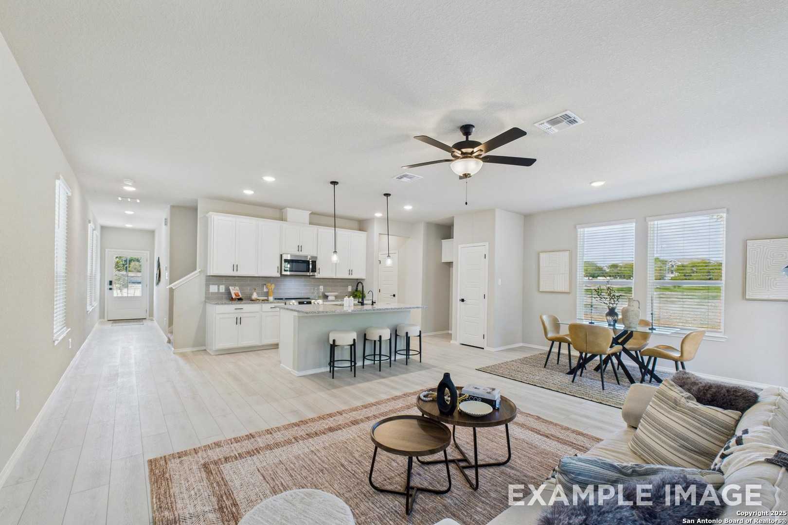 Open-concept living and dining area with modern kitchen island, white cabinets, and ceiling fan in The Charlotte A by Davidson Homes, San Antonio