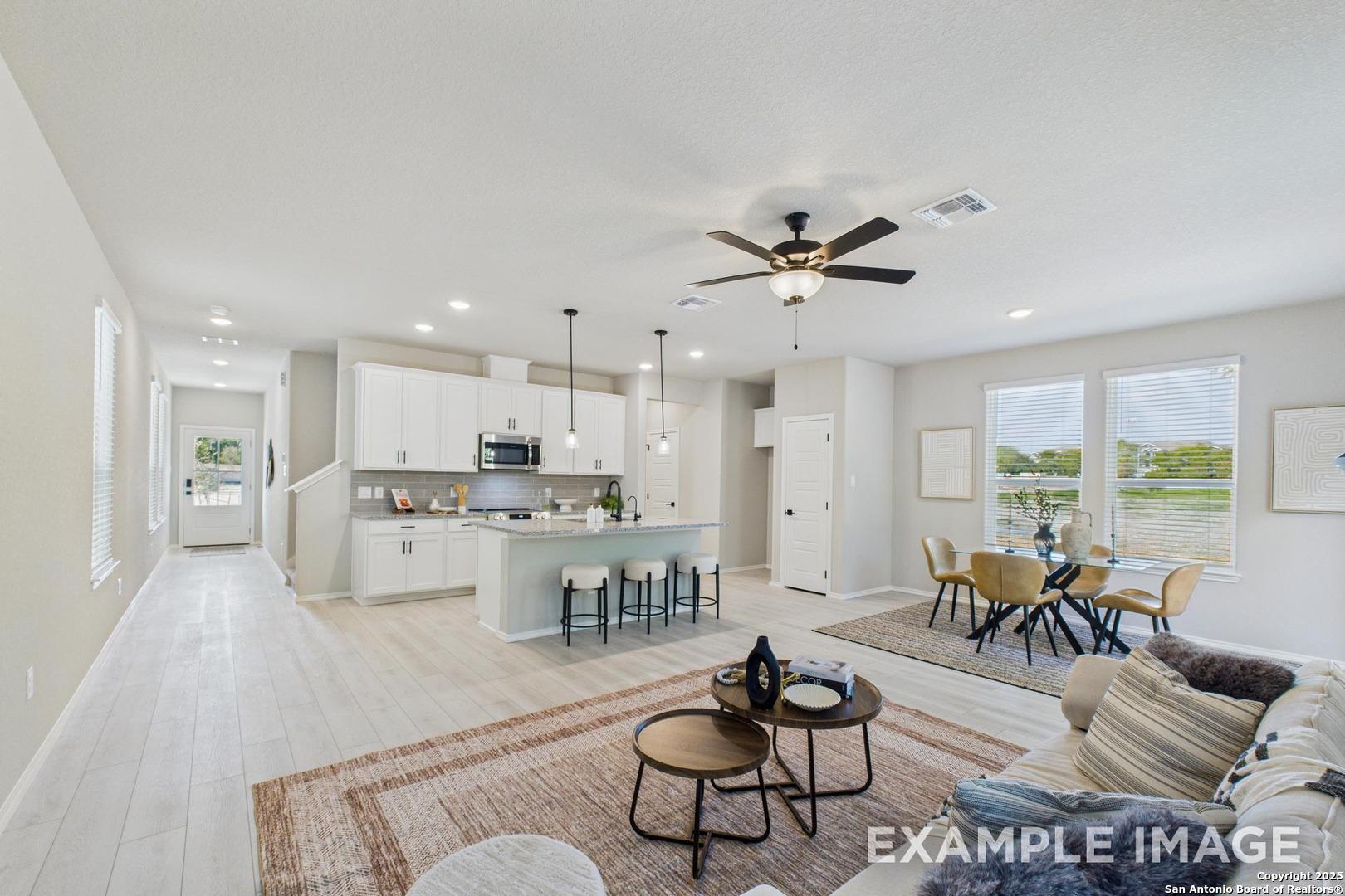 Open-concept living, dining, and kitchen with island bar, white cabinets, and ceiling fan in Davidson Homes The Charlotte B, San Antonio
