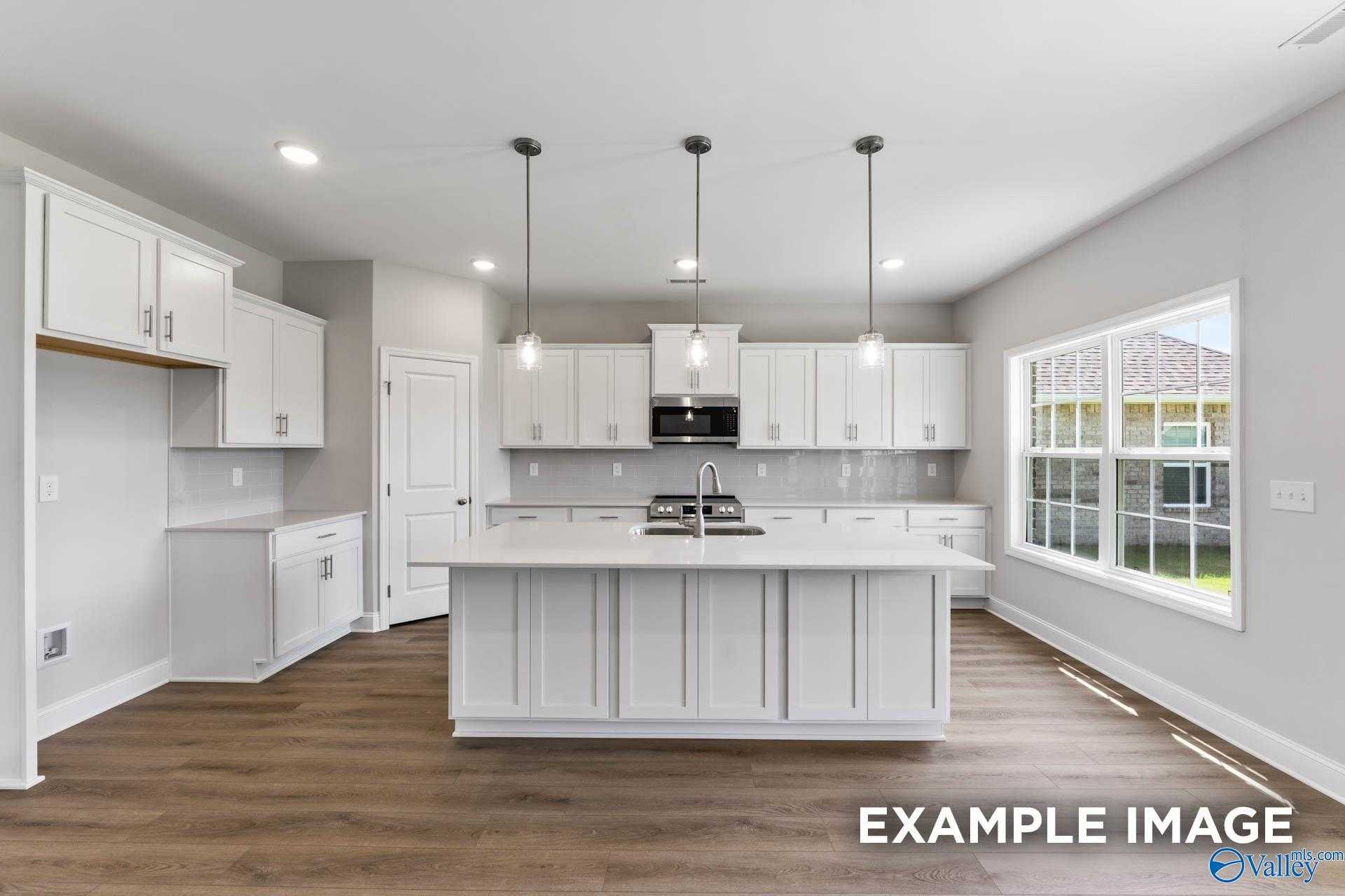Modern white kitchen with large island, stainless appliances, pendant lights, and yard-view window in Davidson Homes The Madison A, Harvest, AL
