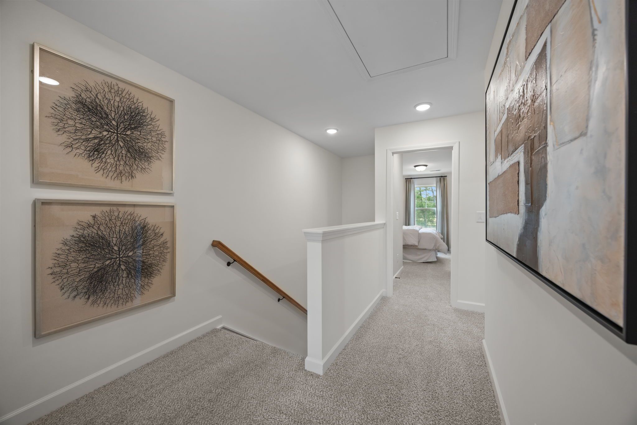 Spacious hallway in Camden Park home, Knightdale NC with abstract tree artworks, wooden railing, beige walls, and carpeted floor