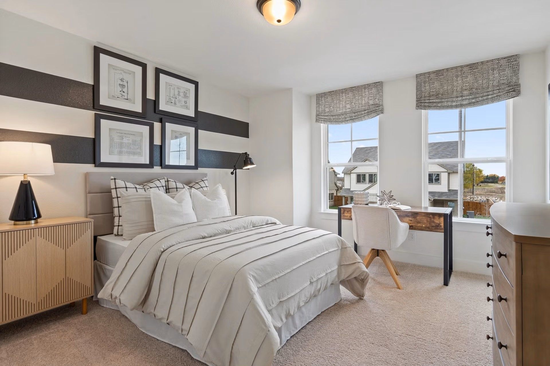Modern bedroom with queen bed, plaid pillows, desk, and window views in Davidson Homes The Wake D, Wylie, Texas