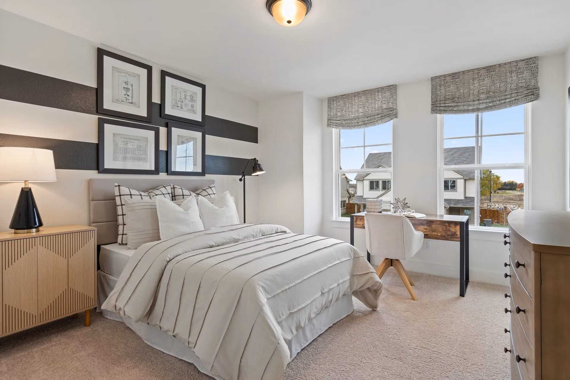 Modern bedroom with queen bed, plaid pillows, desk, and window views in Davidson Homes The Wake D, Wylie, Texas