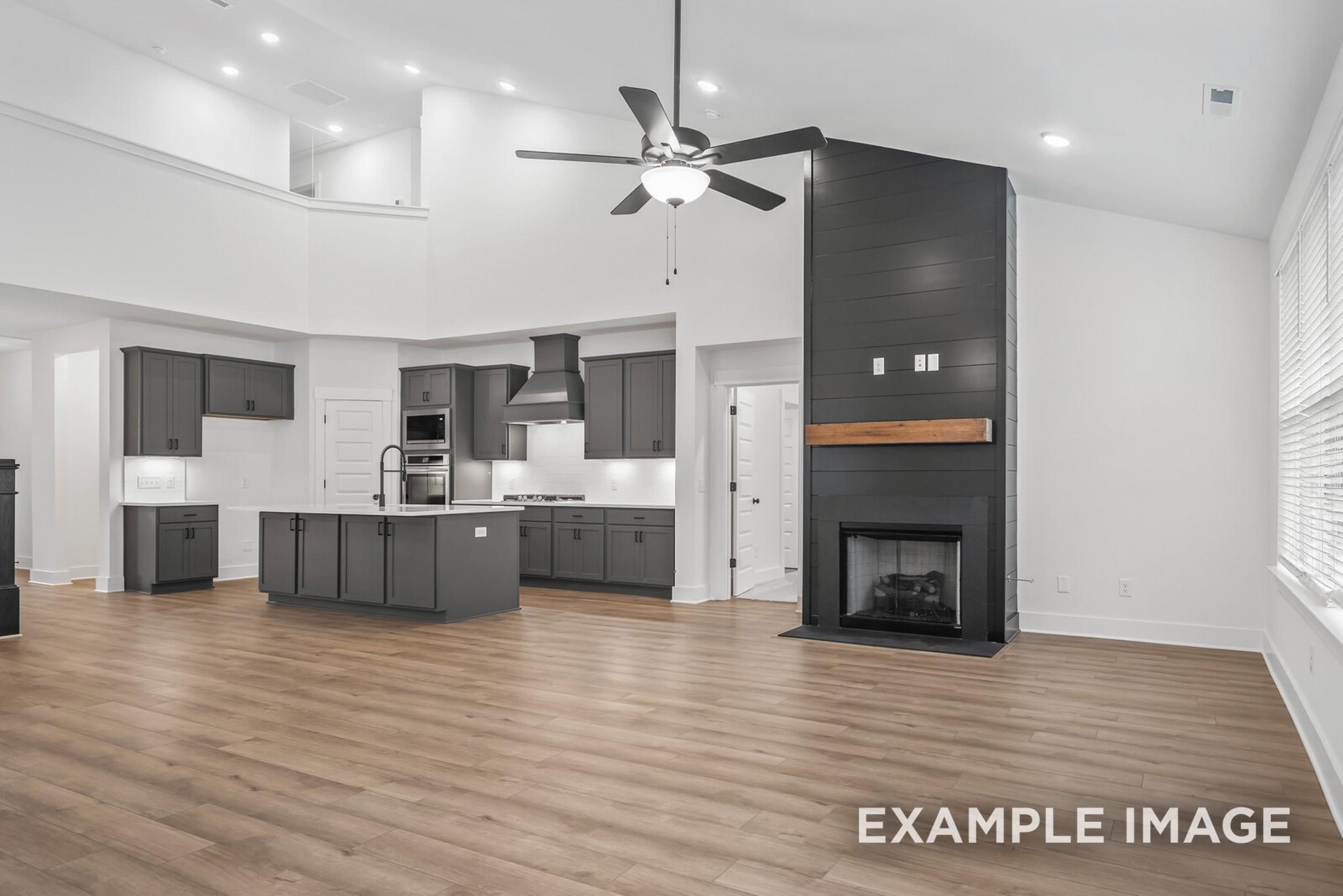 Open-concept kitchen with gray cabinets, large island sink, and adjacent living room featuring sleek black fireplace in 5-bedroom Davidson Homes Ridgeport C, Gallatin, TN