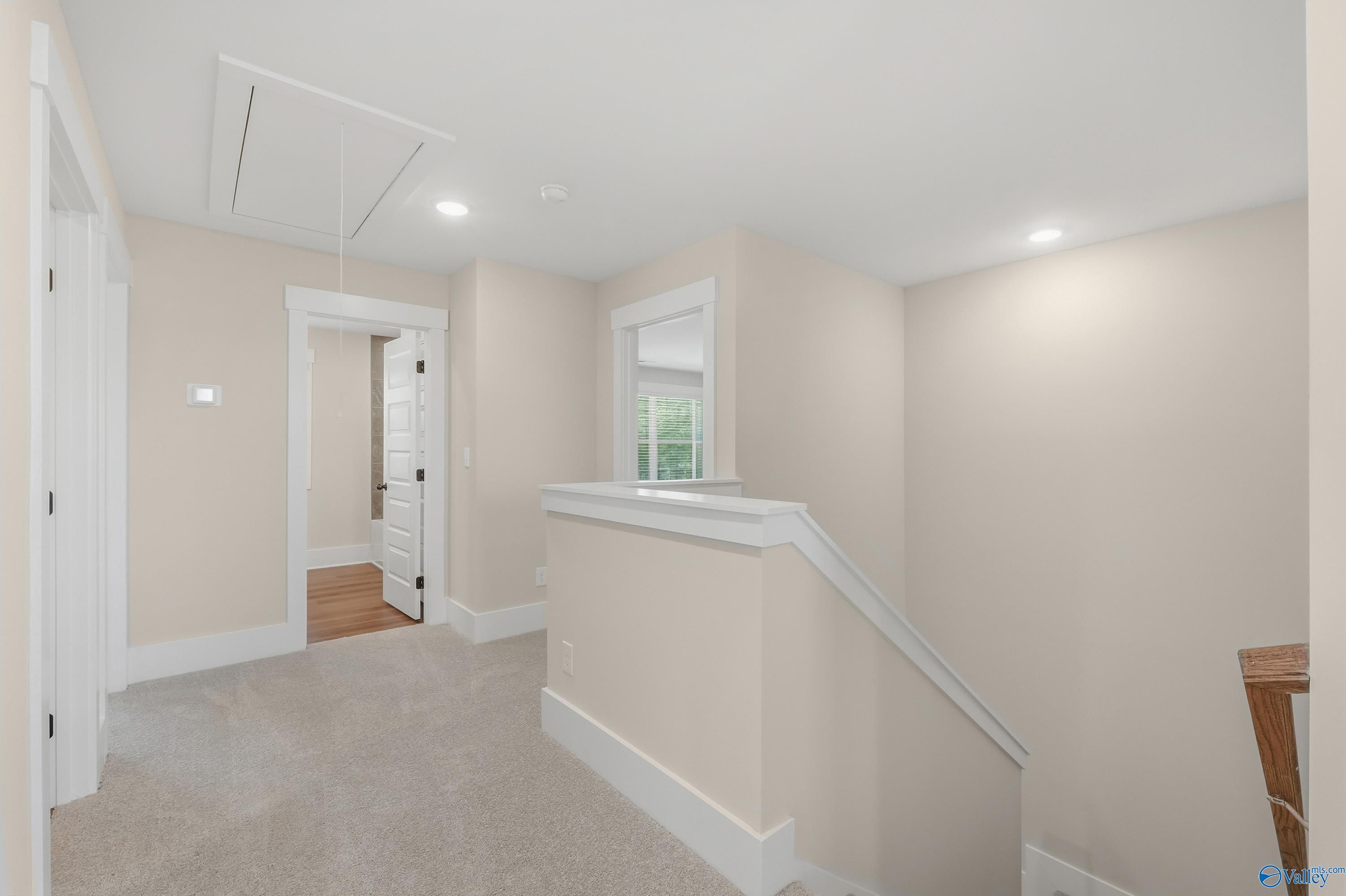 Bright upstairs hallway with beige carpet, white doors, and open stair railing in The Shelby A floor plan, Athens, Alabama