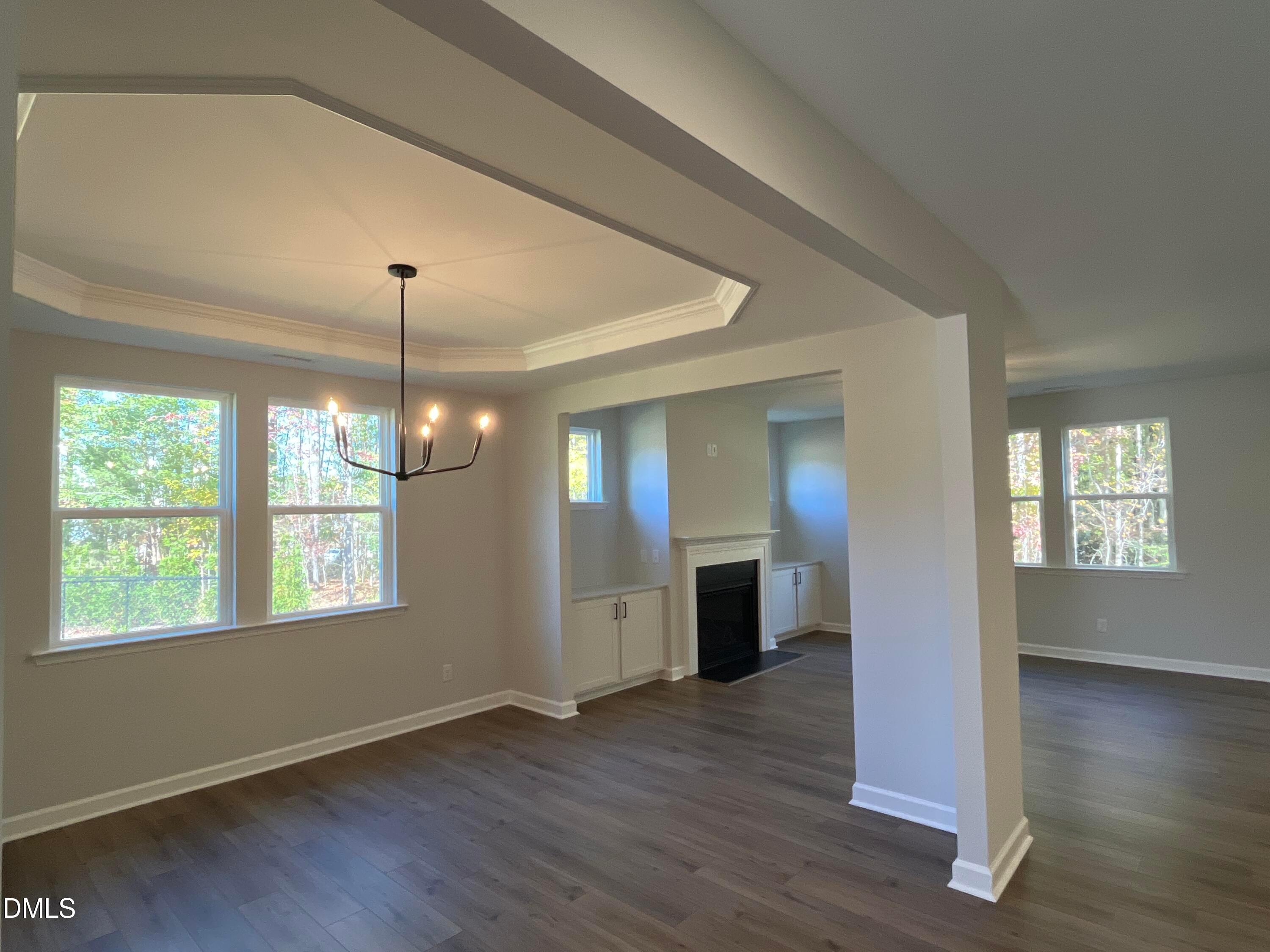 Dining room with tray ceiling, chandelier, and hardwood floors opening to fireplace in Davidson Homes Beech C, Wake Forest, NC