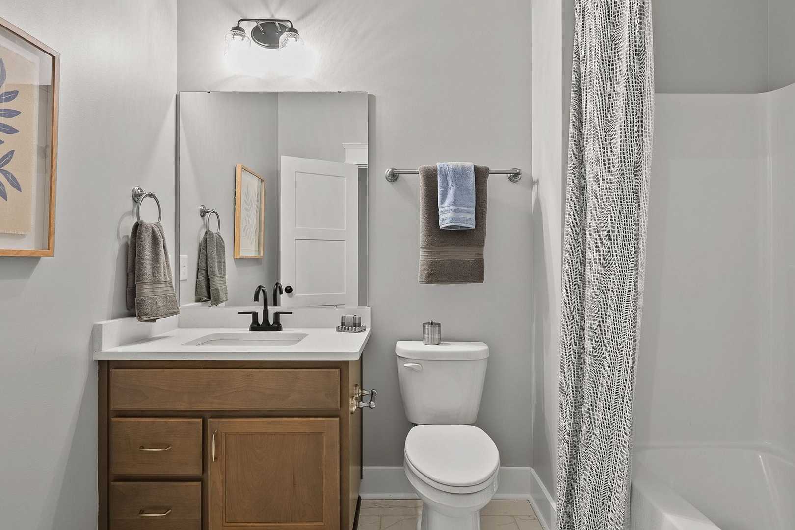 Modern bathroom in The Oxford home with gray walls, wooden vanity, single sink, mirror, toilet, and walk-in shower