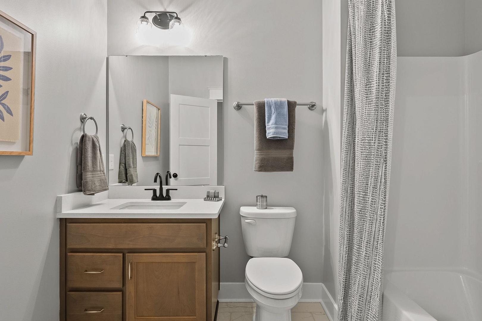 Modern bathroom in The Oxford home with gray walls, wooden vanity, single sink, mirror, toilet, and walk-in shower
