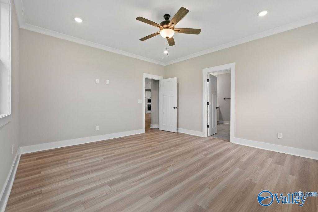 Spacious bedroom with light hardwood floors, neutral walls, ceiling fan, and en-suite bathroom door in Evermore Homes The Oxford, Owens Cross Roads, AL