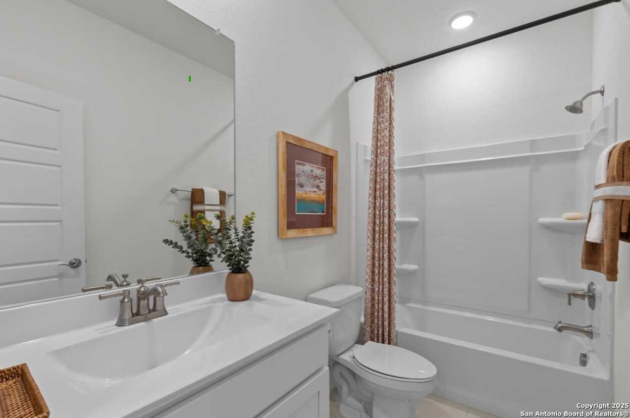 Bright white secondary bathroom with bathtub, patterned shower curtain, and double sink vanity in Davidson Homes The Daphne J, Elmendorf, Texas