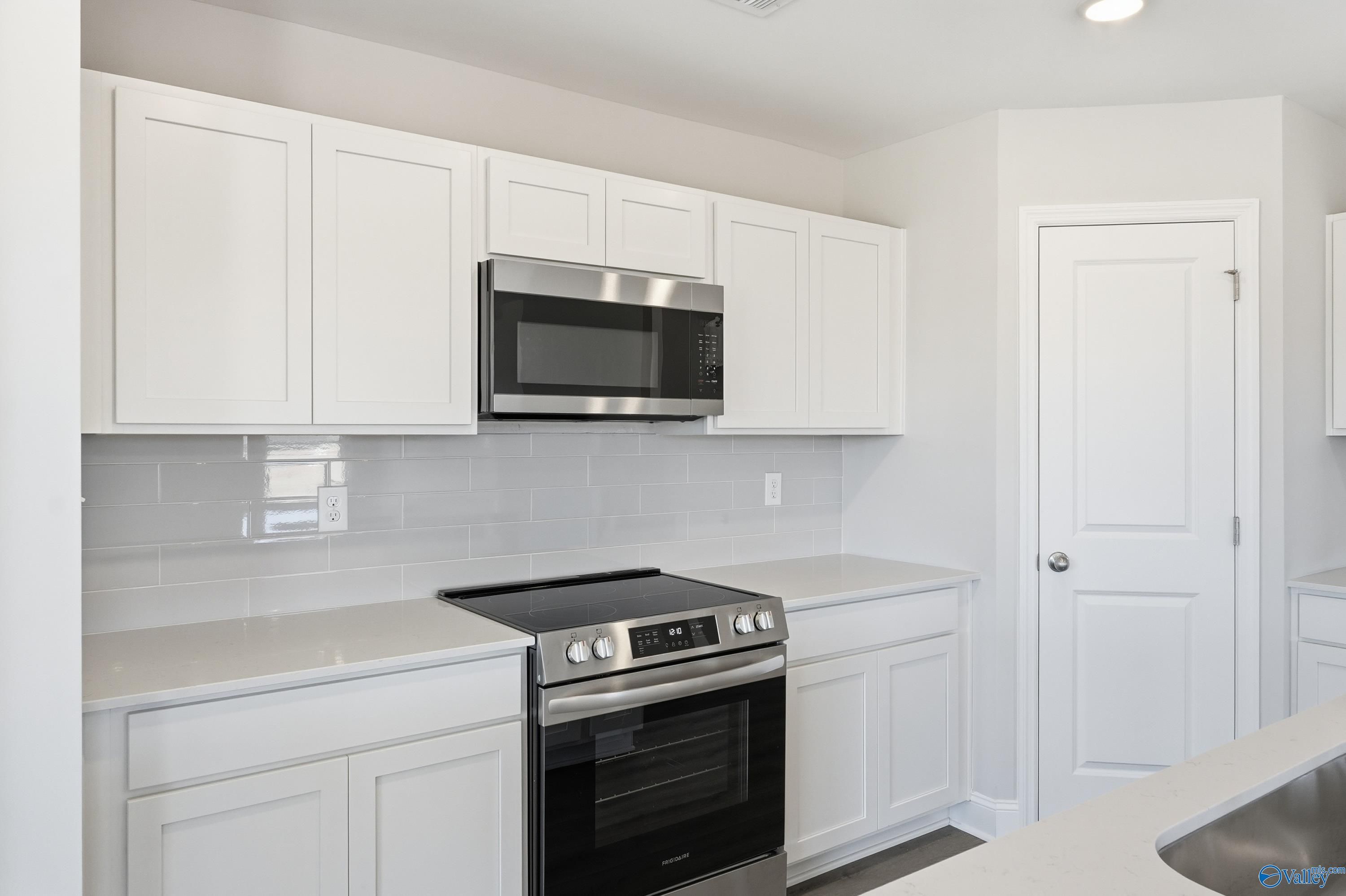 Modern white kitchen with stainless steel appliances, subway tile backsplash, and quartz counters in Davidson Homes The Franklin, New Market, Alabama