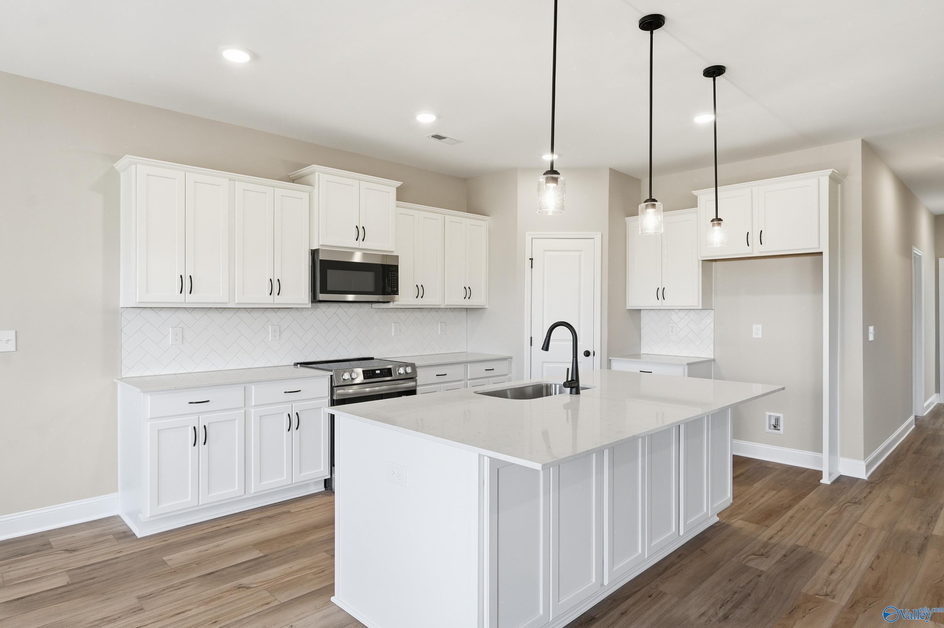 Modern white kitchen with quartz island, stainless appliances, subway tile backsplash in Davidson Homes The Rockford, Harvest, AL