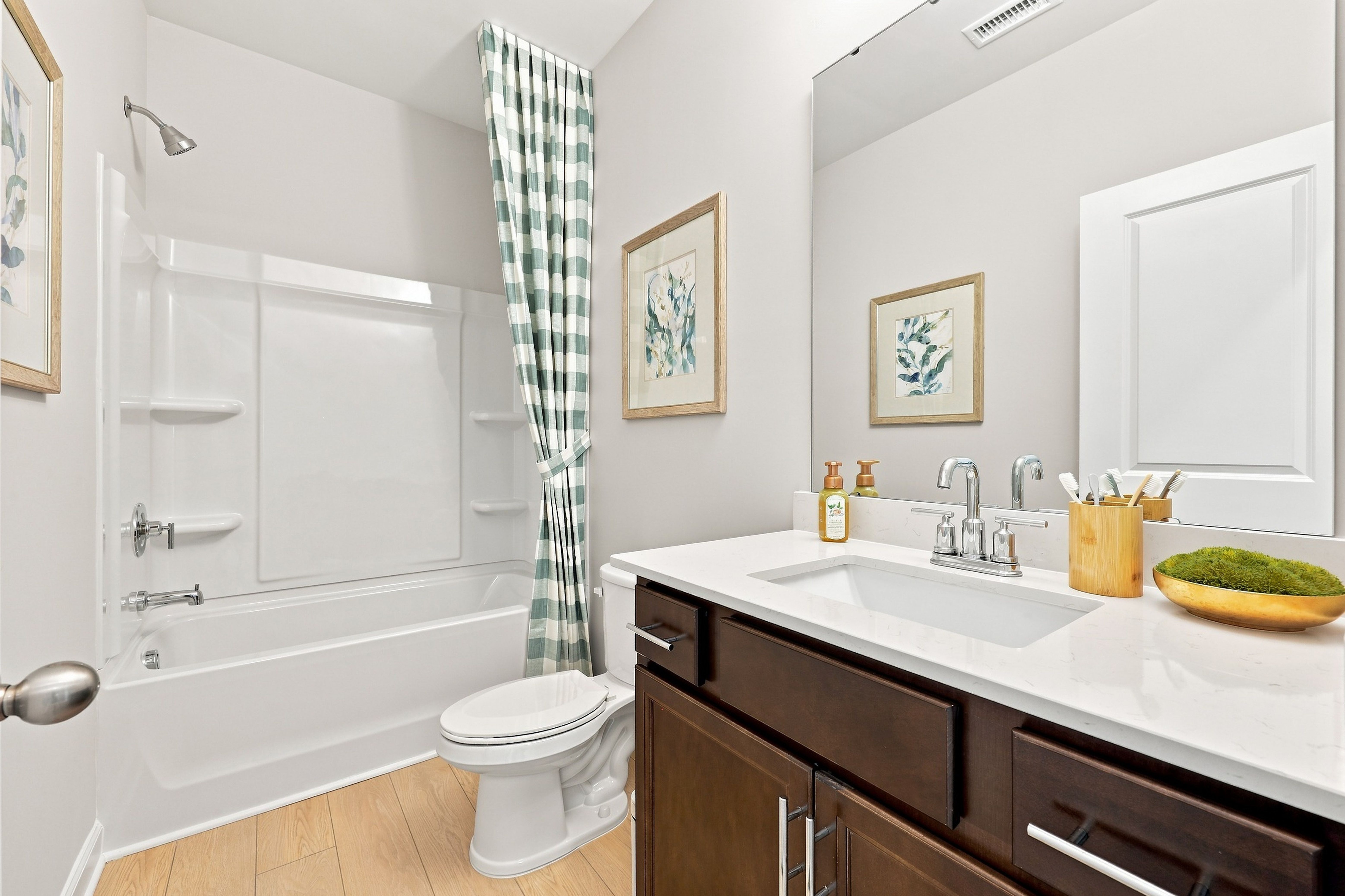 Modern bathroom in The Daphne D featuring a dark wood vanity, white quartz countertop, and tub-shower combo.