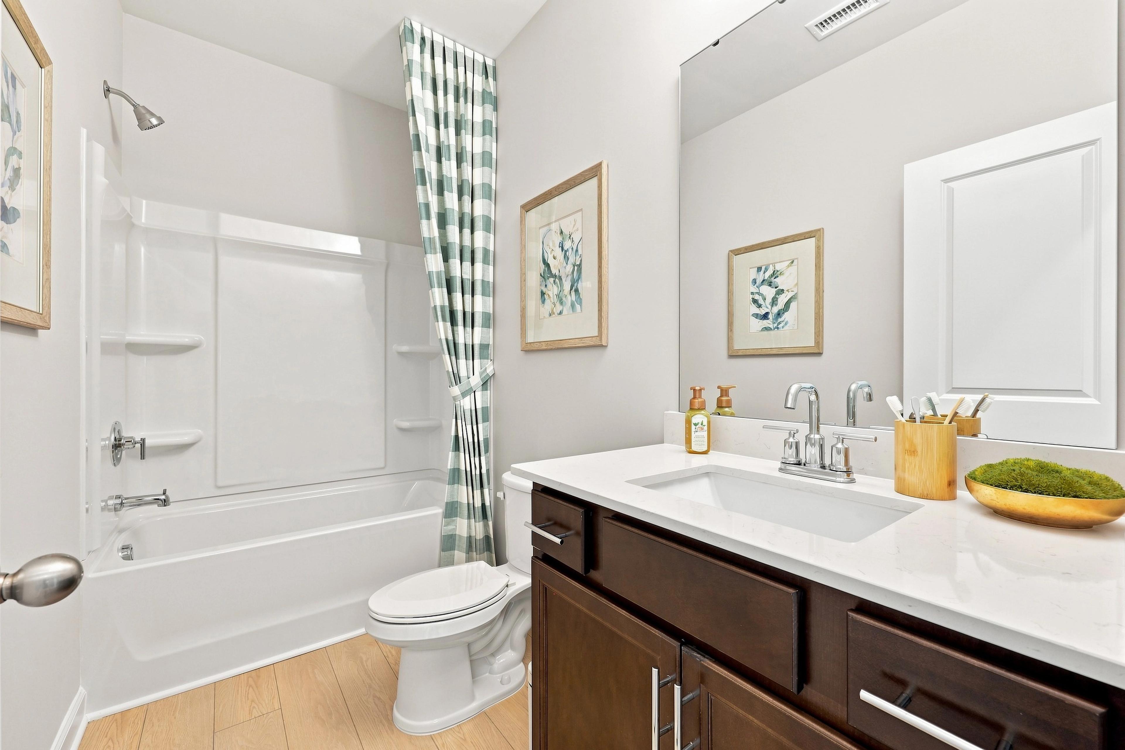 Modern bathroom in The Daphne D featuring a dark wood vanity, white quartz countertop, and tub-shower combo.