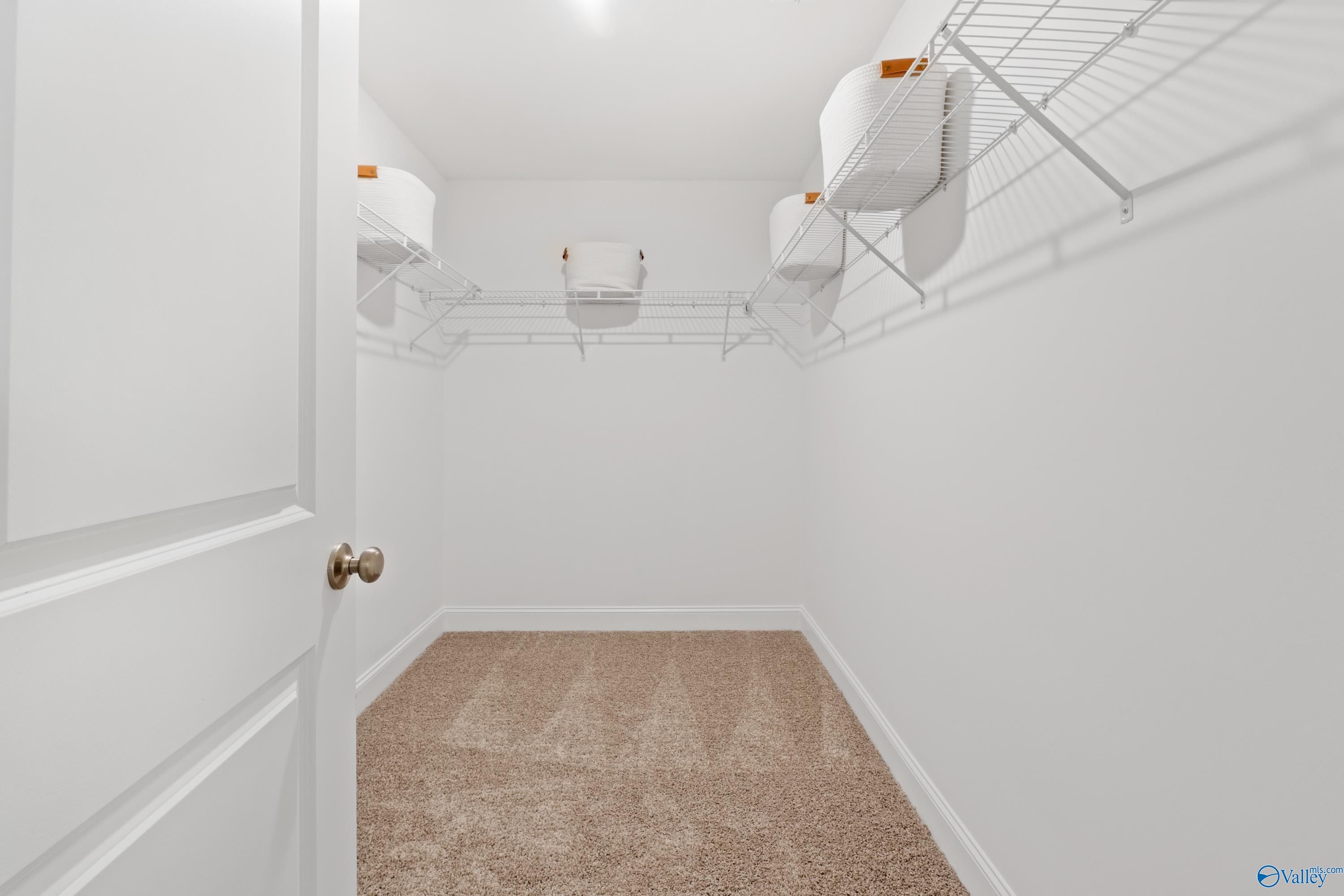 Walk-in closet with wire shelving, hanging rods, and orange storage bins on beige carpet in Davidson Homes The Camden, Huntsville
