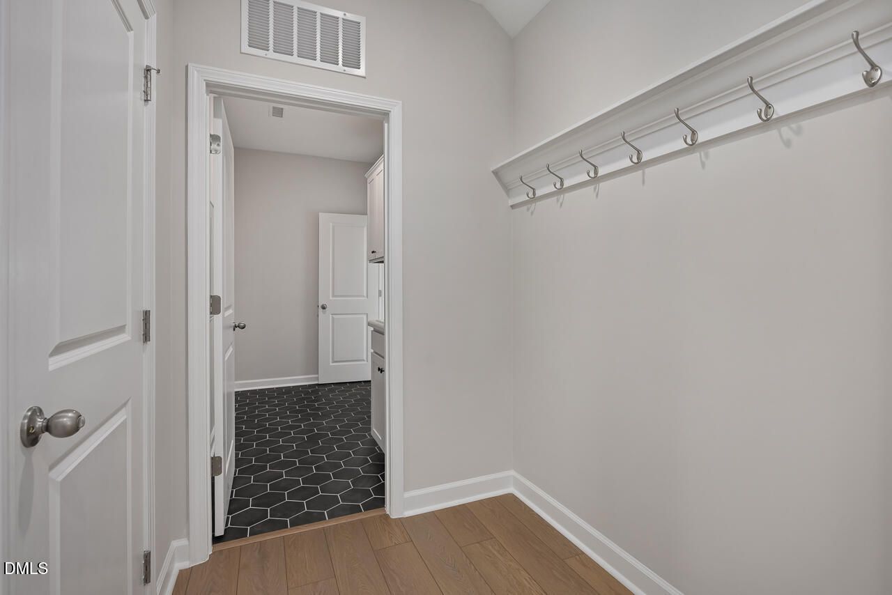 Mudroom with wall-mounted coat hooks and hardwood floors leading to a tiled laundry room in The Ashport L, Wake Forest, NC.