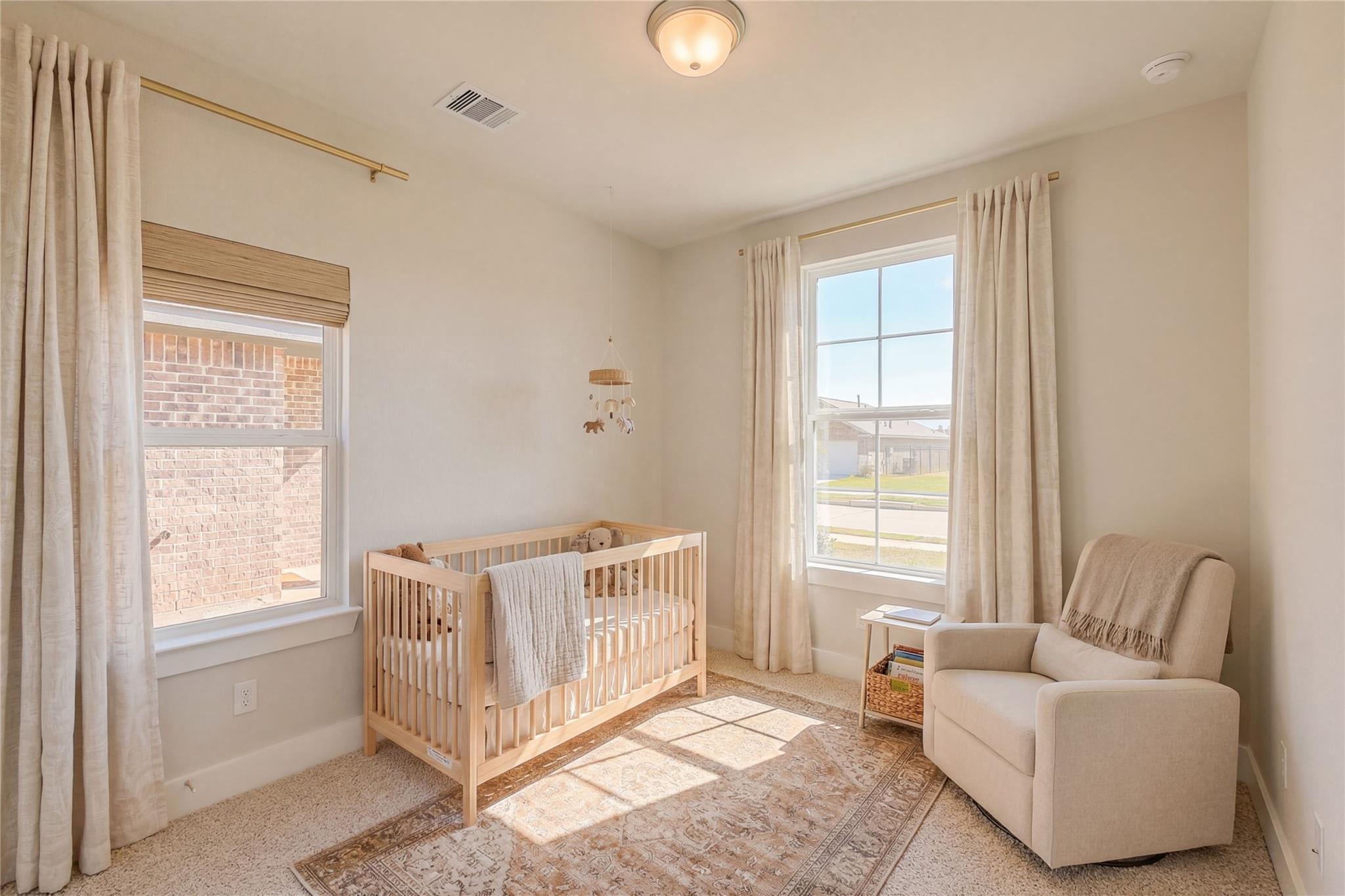 Cozy nursery with wooden crib, teddy bear, rocking chair, and hanging mobile in Davidson Homes The Luna L, Sunterra, Katy, Texas