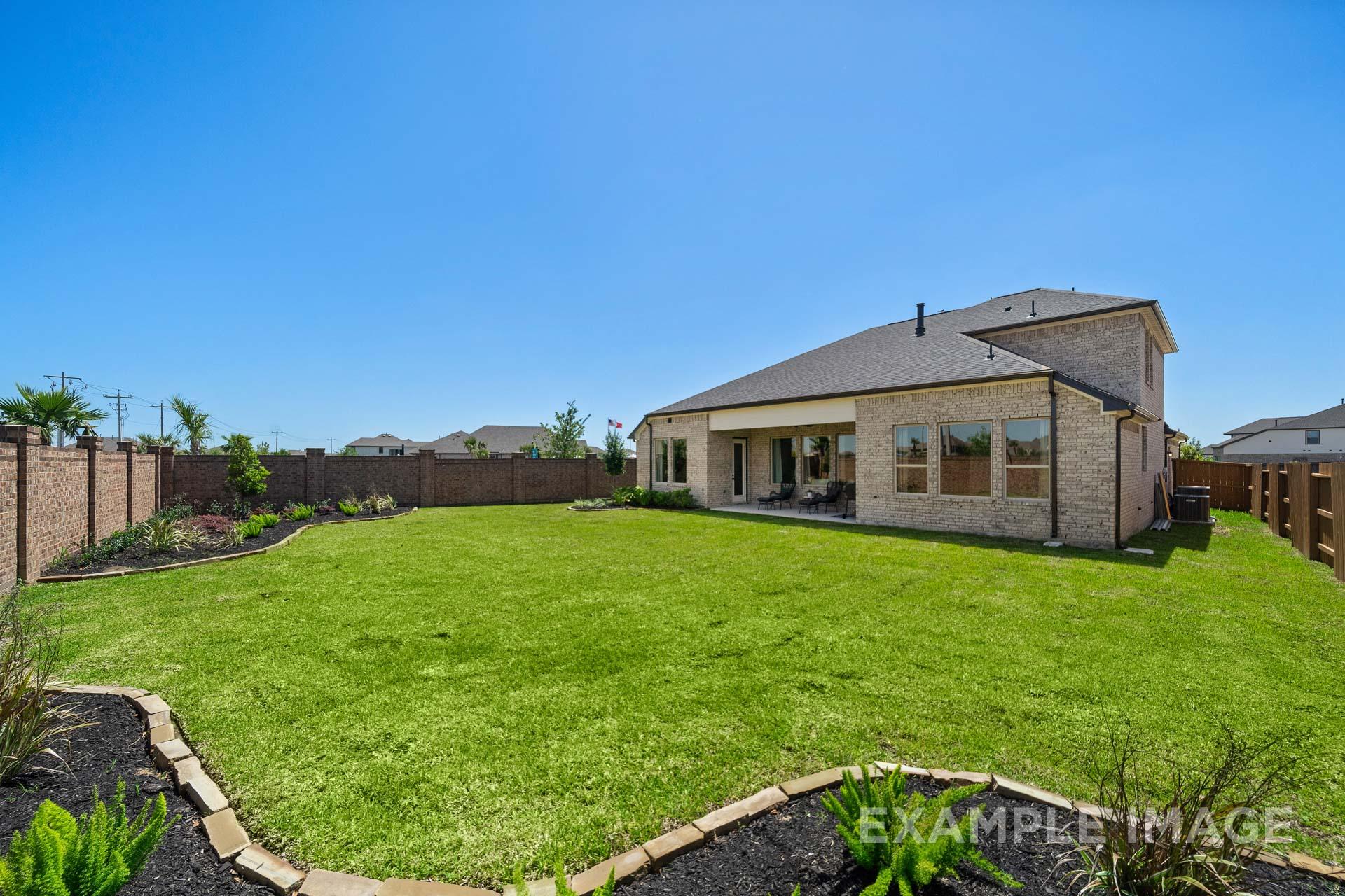 Rear elevation of The Edward B single-story home with 3-car garage, brick exterior, covered patio, and lush green yard
