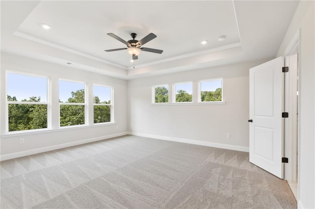 Spacious upstairs bedroom with large windows overlooking trees, ceiling fan, and carpeted floors in Davidson Homes The Hickory B, Buford, GA