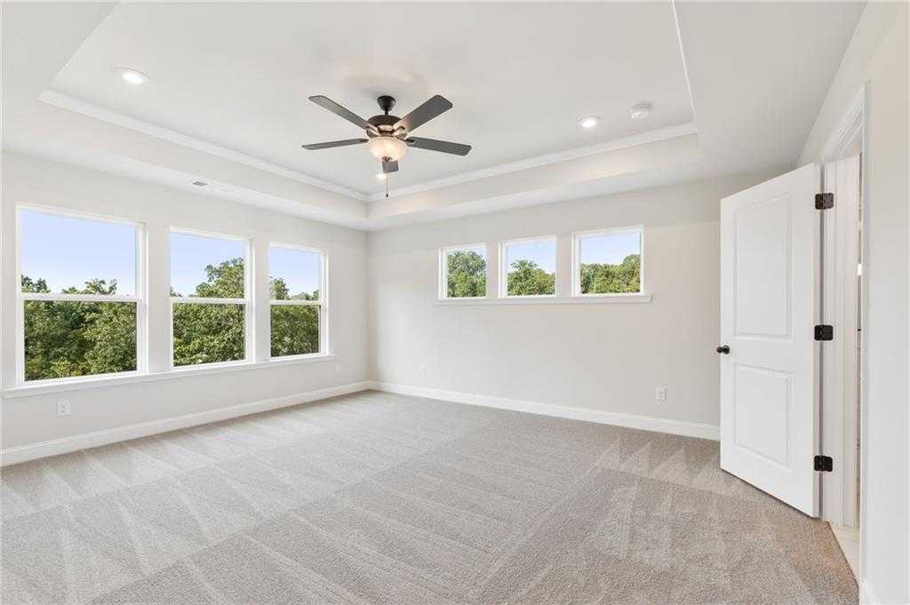 Spacious upstairs bedroom with large windows overlooking trees, ceiling fan, and carpeted floors in Davidson Homes The Hickory B, Buford, GA