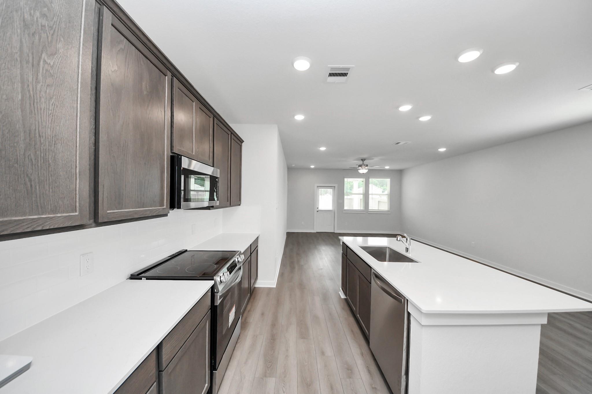 Modern kitchen with white quartz island, dark cabinets, and stainless appliances in The Brazos F floor plan, Cleveland, TX.