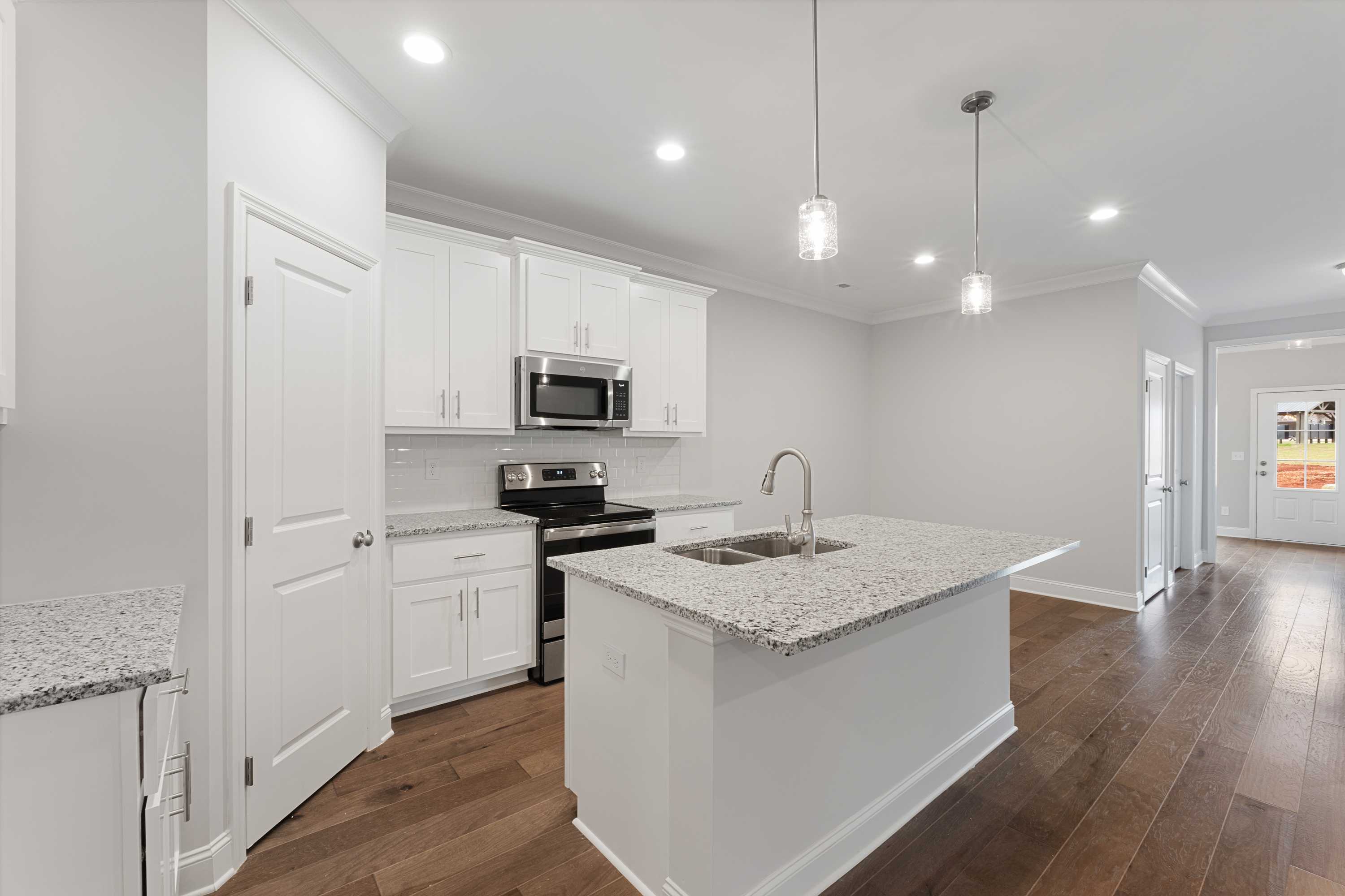 Spacious Copeland B kitchen featuring white shaker cabinets, granite island sink, stainless appliances, and hardwood floors