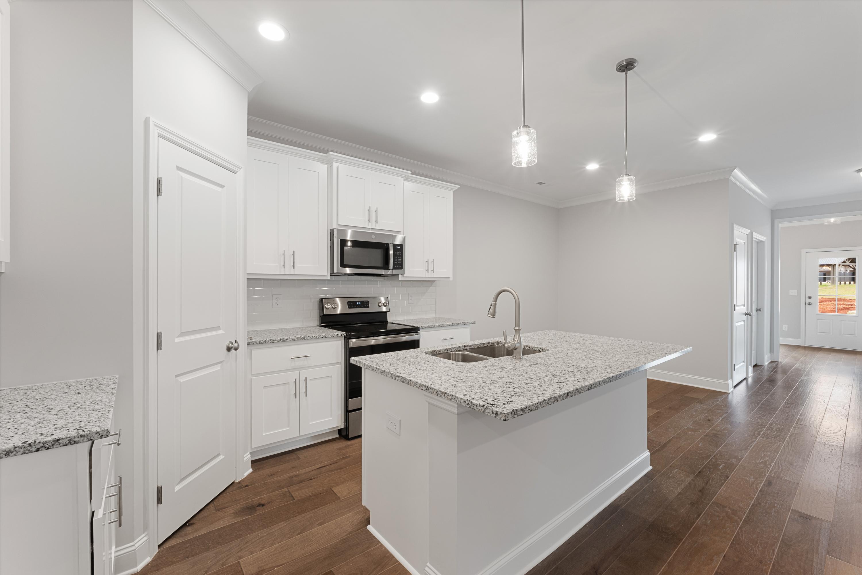 Modern kitchen in The Copeland C with white shaker cabinets, granite island, stainless appliances, and open layout