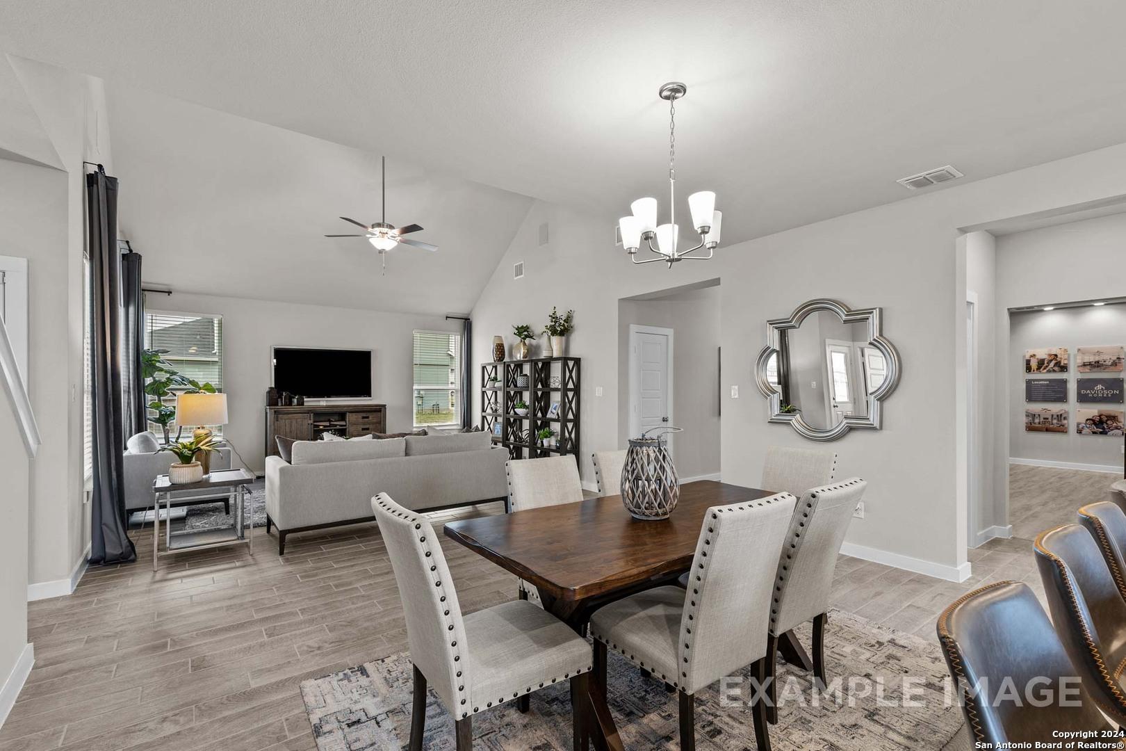 Open-concept living dining area with wooden table, gray sofa, chandelier in Davidson Homes The Collin A, Seguin, Texas
