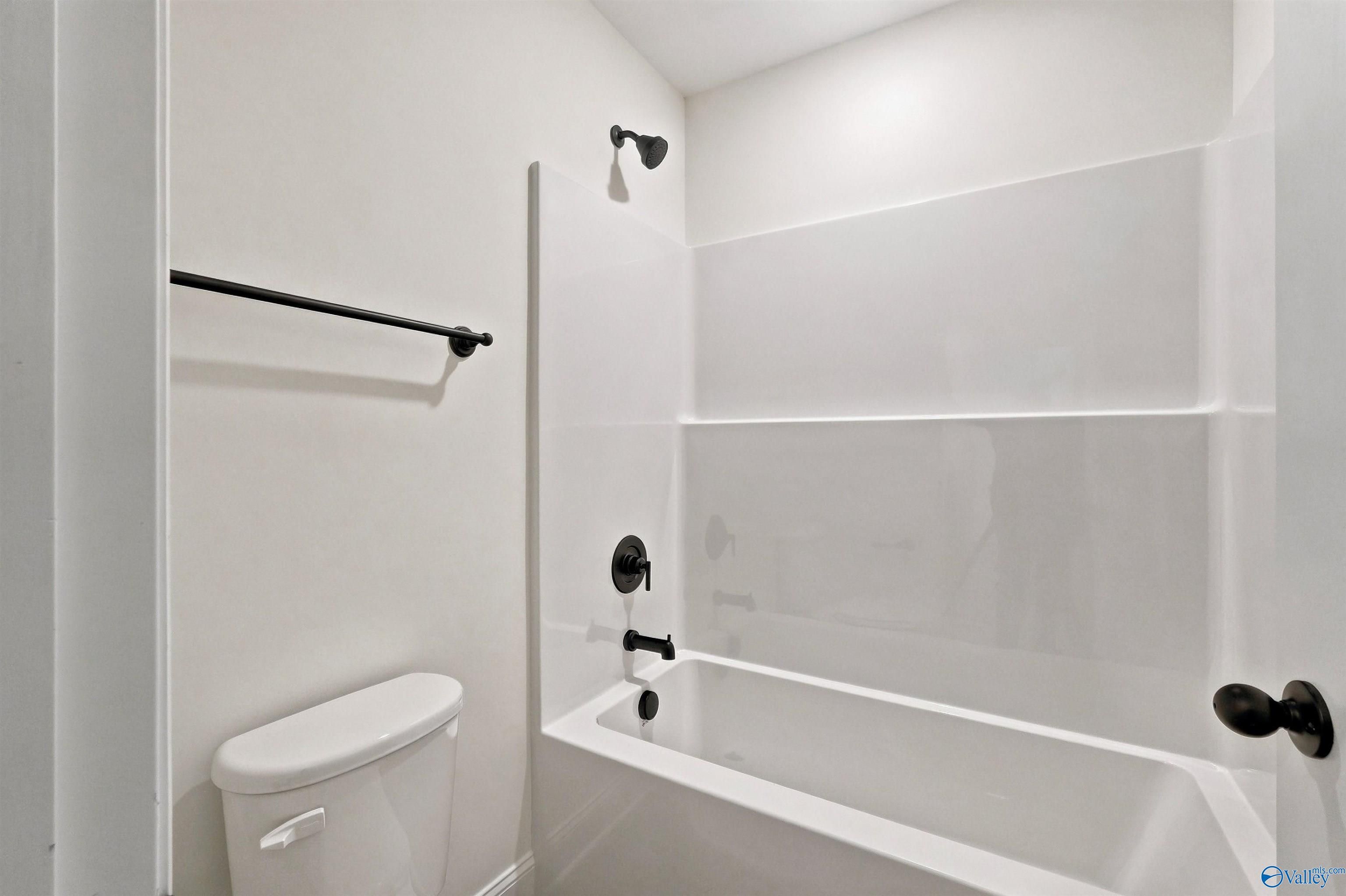 Modern bathroom with white tub-shower combo and sleek black fixtures in The Chelsea C home at Creek Grove, New Market, AL.