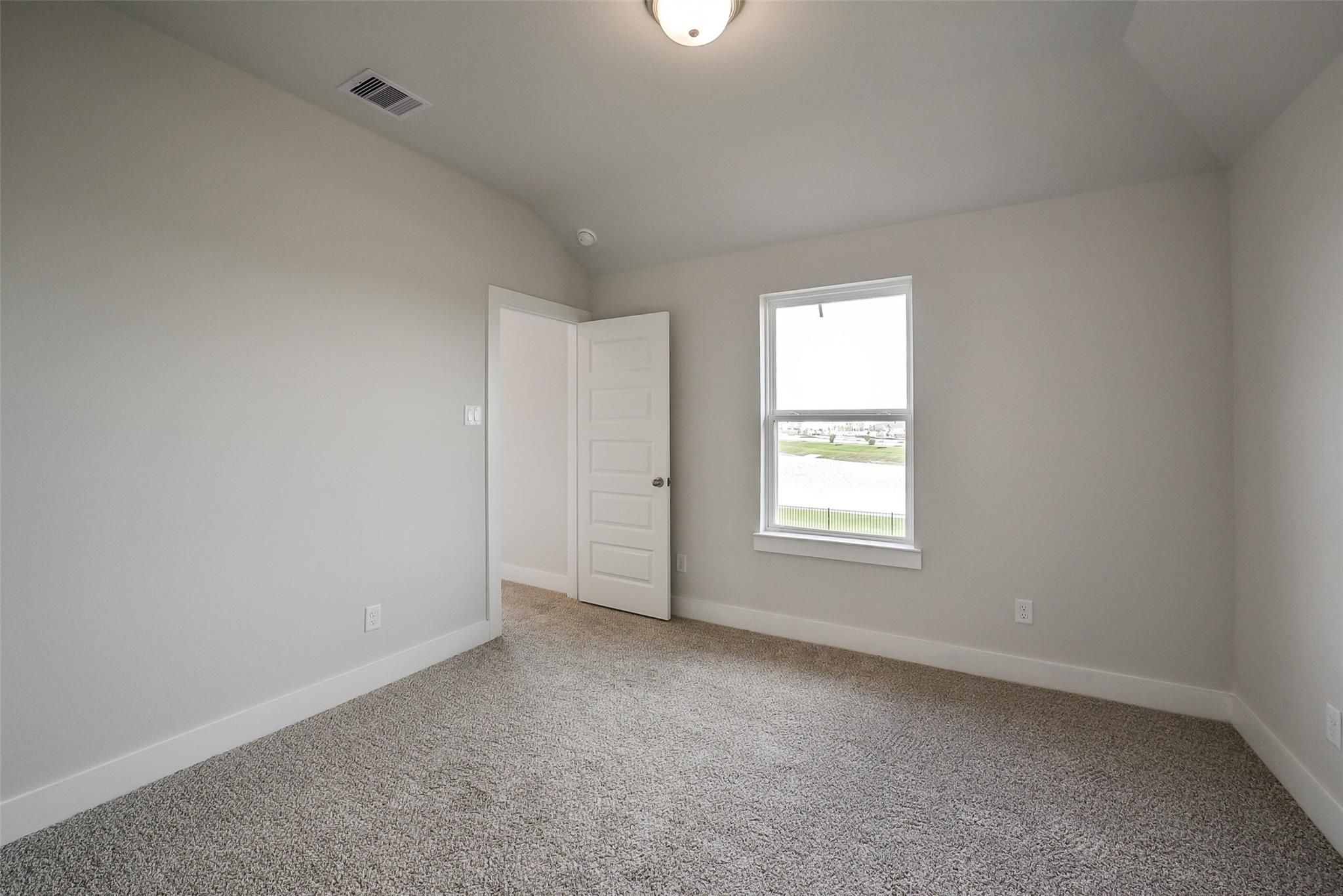 Neutral-toned secondary bedroom with carpet flooring, interior door, and window view in Davidson Homes The Philip B, Rosharon, Texas