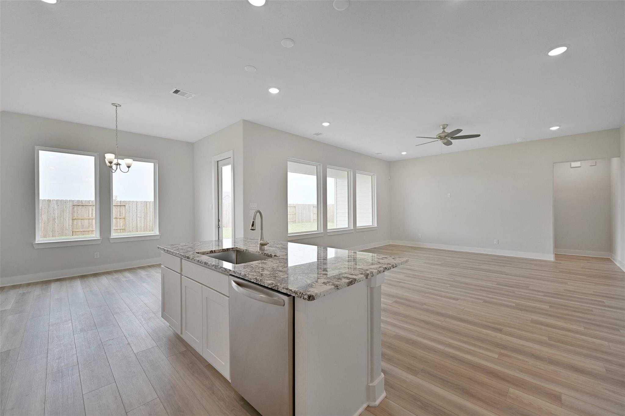 Modern open-concept kitchen with white cabinets, granite island, stainless dishwasher, and large windows in Davidson Homes The Edward A, Lago Mar, Texas City