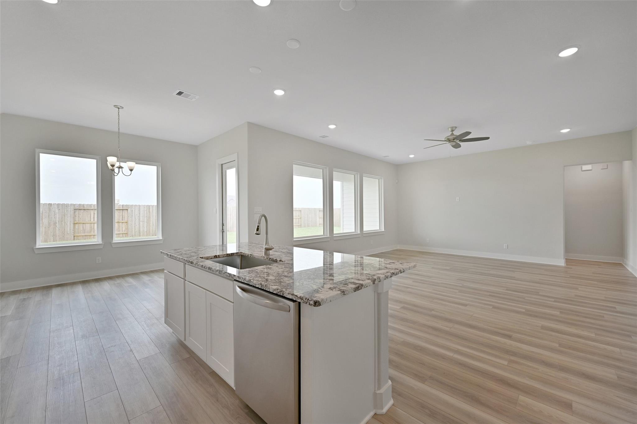 Open-concept kitchen with granite island, white shaker cabinets, stainless dishwasher, and adjacent living area in Davidson Homes The Edward A, Lago Mar, Texas City