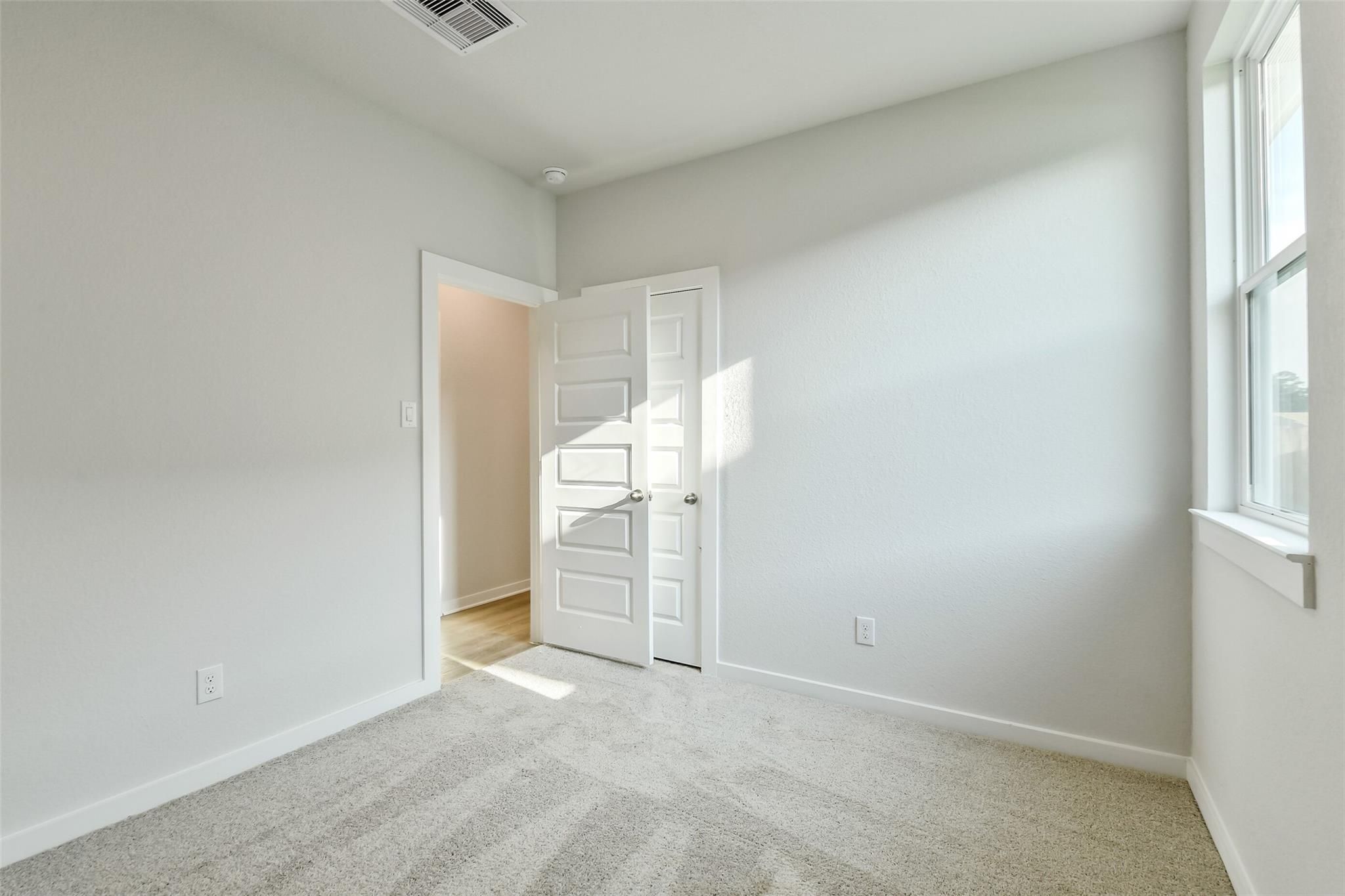 Bright empty bedroom with light gray walls, beige carpet, open closet door, and sunny window in Davidson Homes The Colorado F, Cleveland, Texas