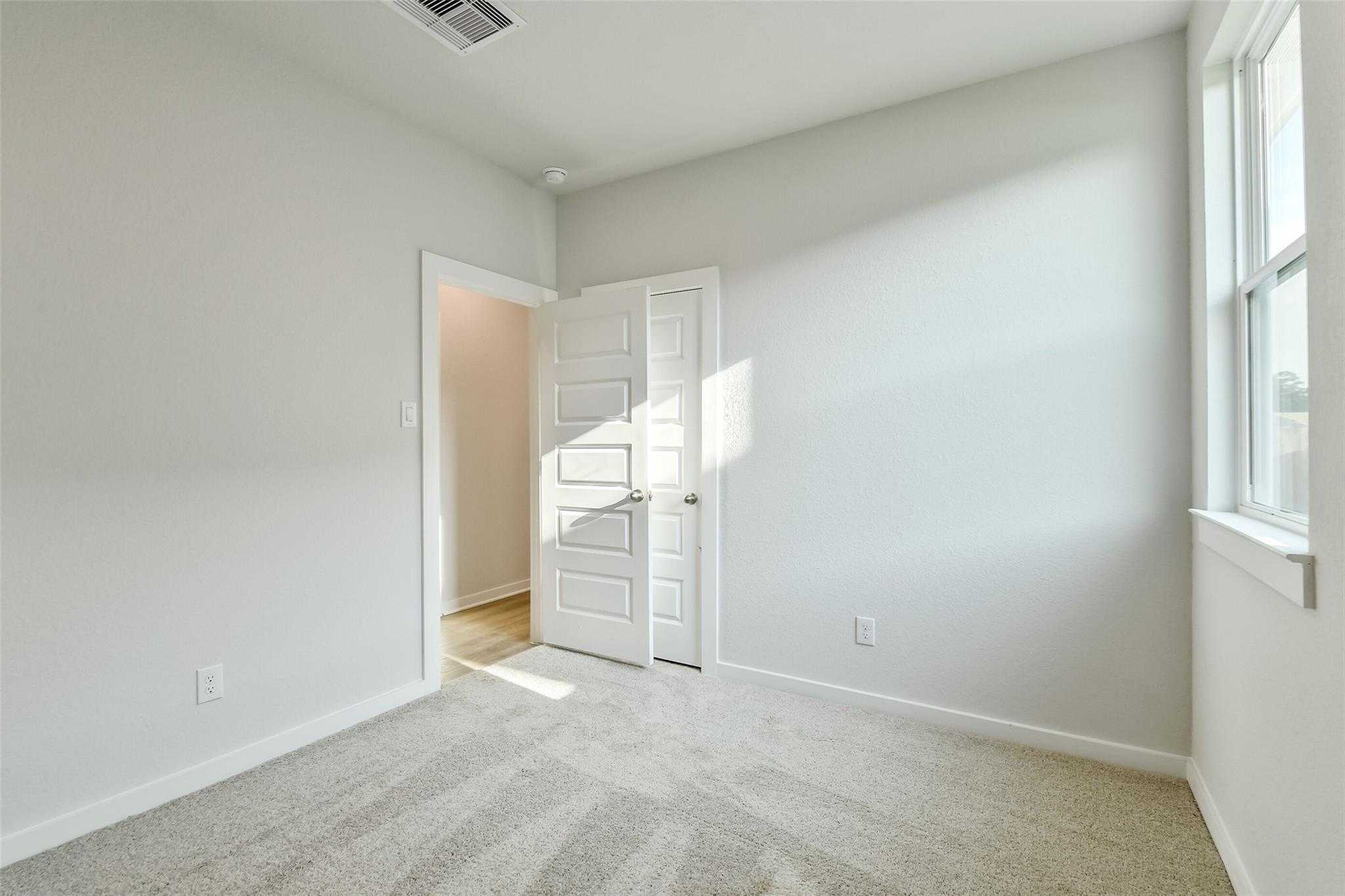 Bright empty bedroom with light gray walls, beige carpet, open closet door, and window in Davidson Homes The Colorado F, Cleveland, Texas