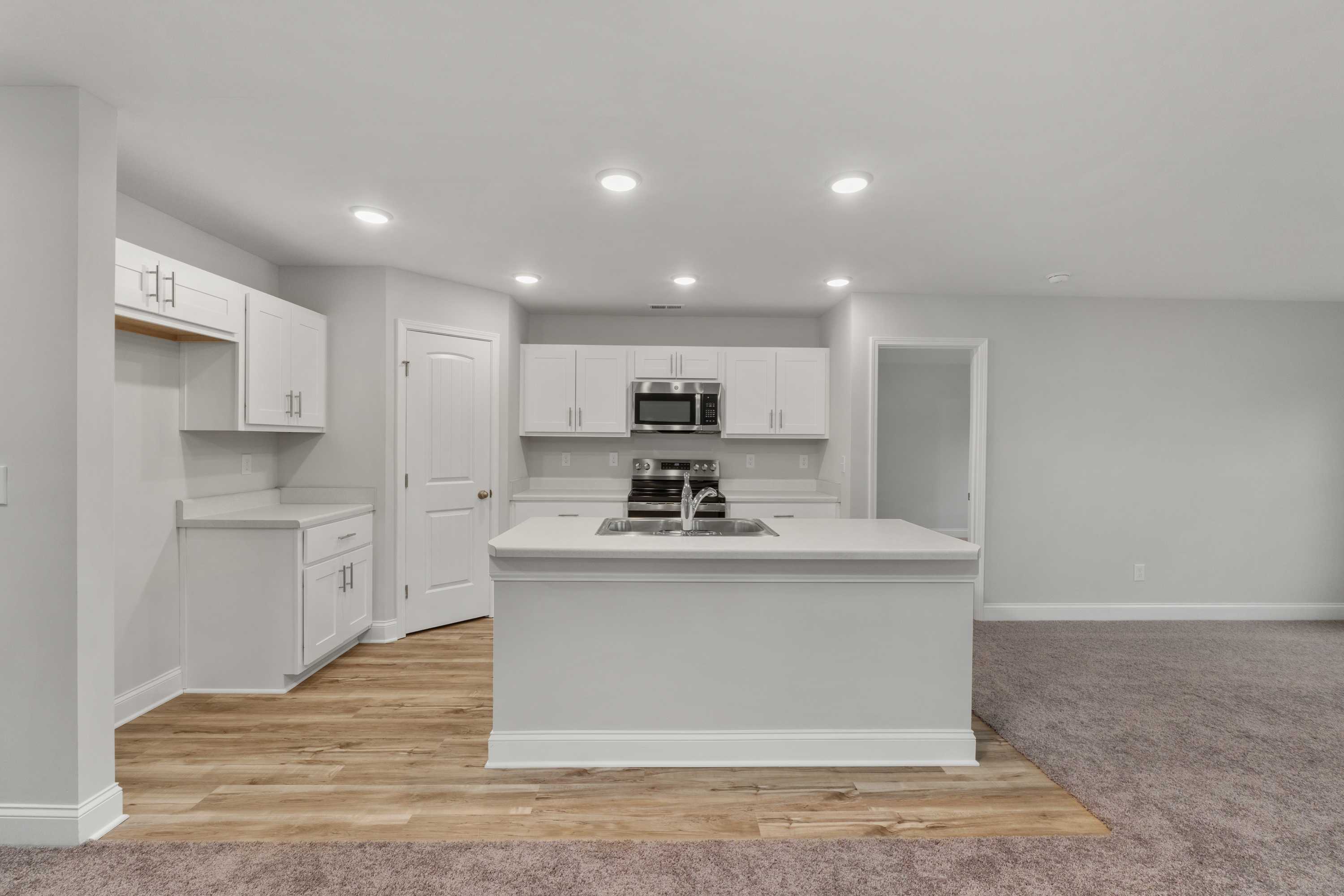 Modern white kitchen in Collins Lane Meridianville AL home with large center island, stainless appliances, hardwood floors