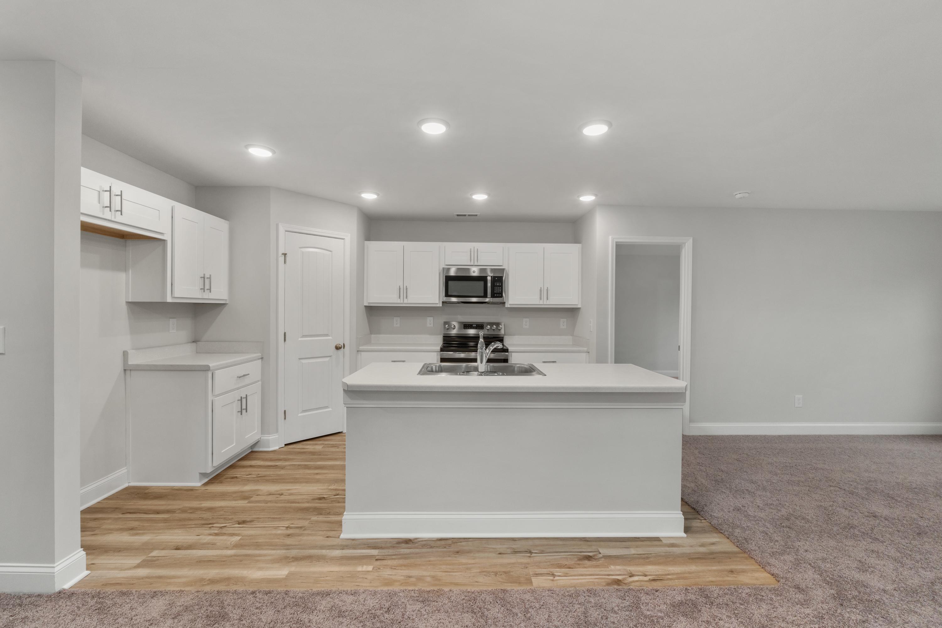 Modern white kitchen in Collins Lane Meridianville AL home with large center island, stainless appliances, hardwood floors