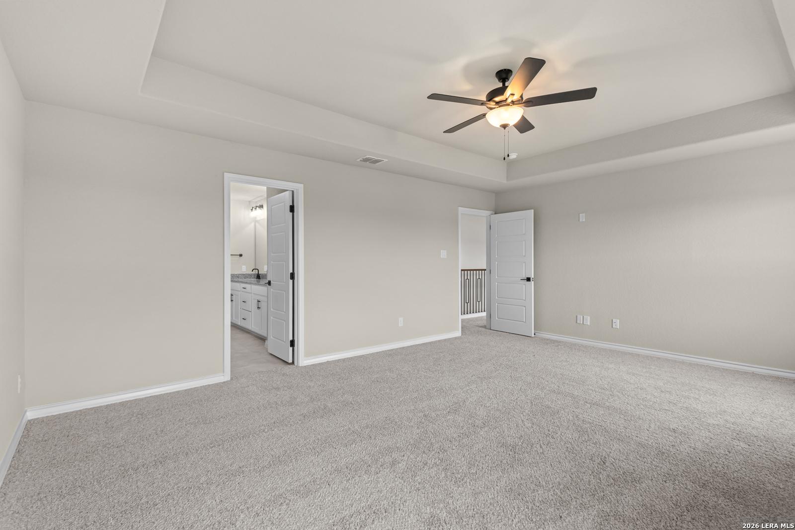 Spacious primary bedroom with tray ceiling and ceiling fan in The Danbury H floor plan at Potranco Oaks, Castroville.