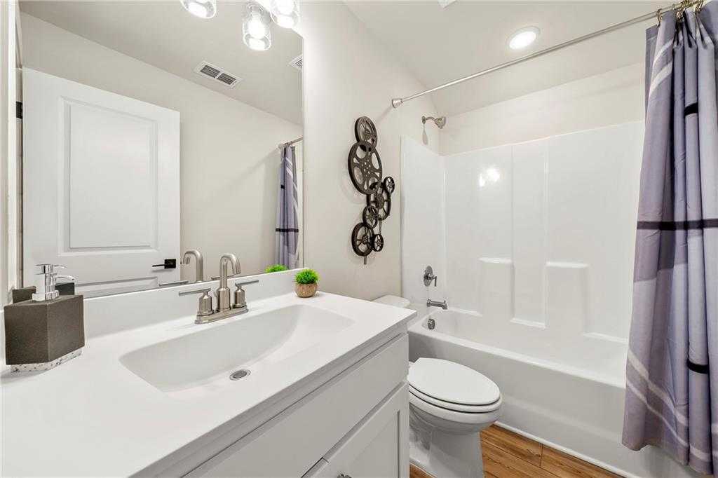 Bright white guest bathroom with single vanity sink, soaking tub, purple shower curtain, and hardwood floors in Davidson Homes The Hickory B, Riverwood, Dallas, Georgia