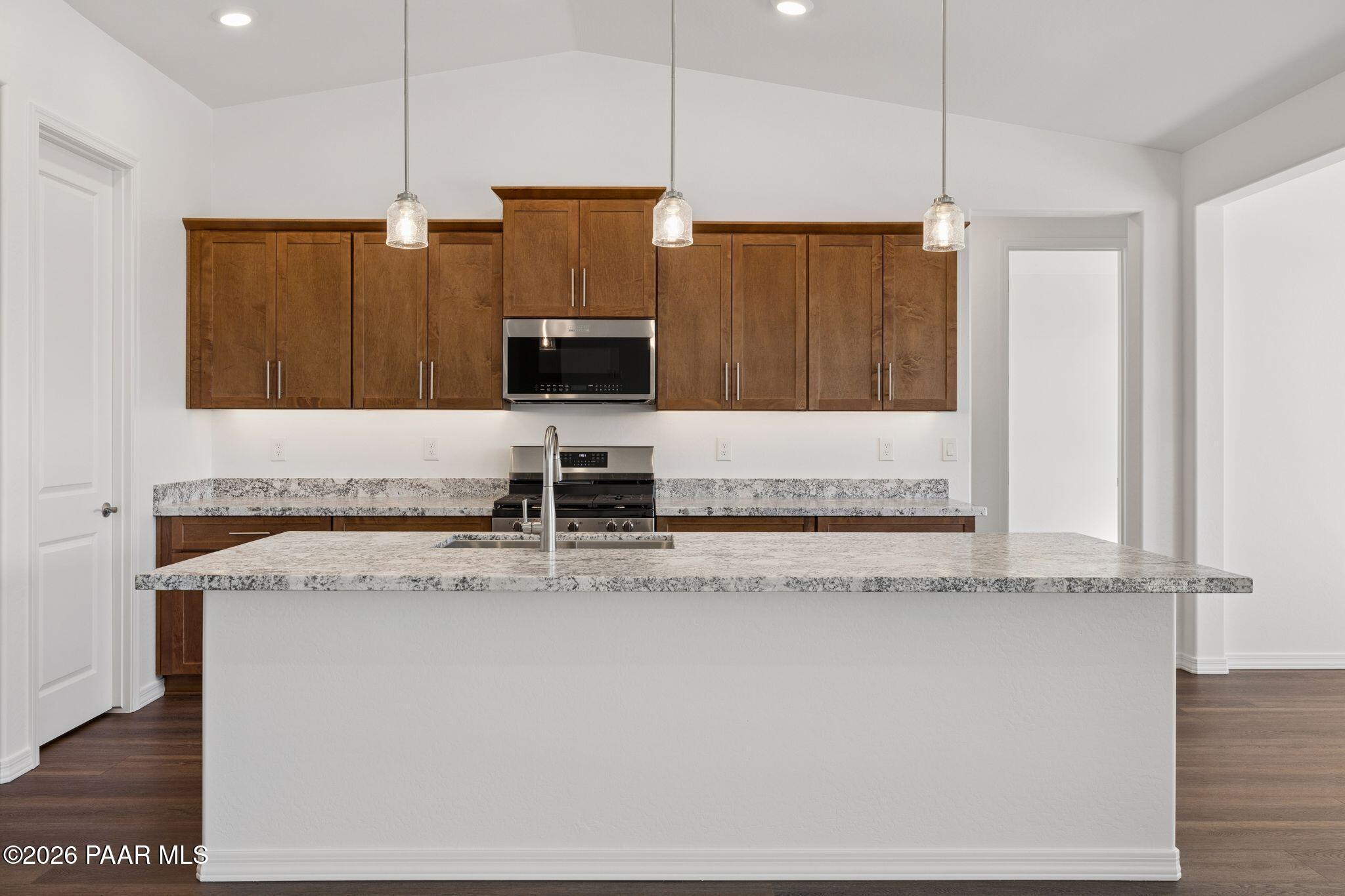 Modern kitchen with granite island, stainless appliances, wooden cabinets, and pendant lights in Davidson Homes The Monarch A, Prescott AZ