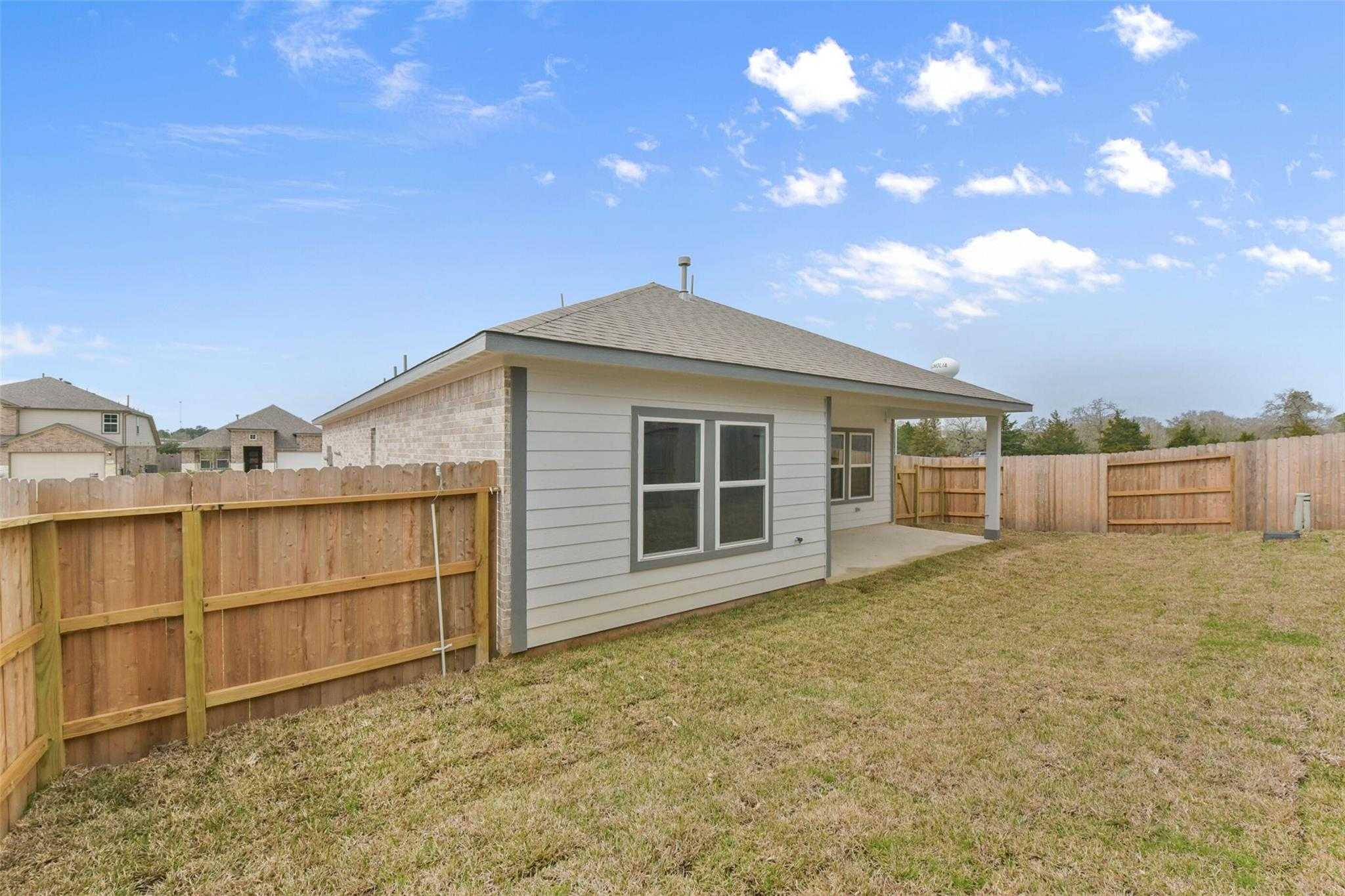 Side view of The Laguna B single-story home with covered patio, double windows, and fenced grassy backyard in Windmill Estates, Magnolia, Texas