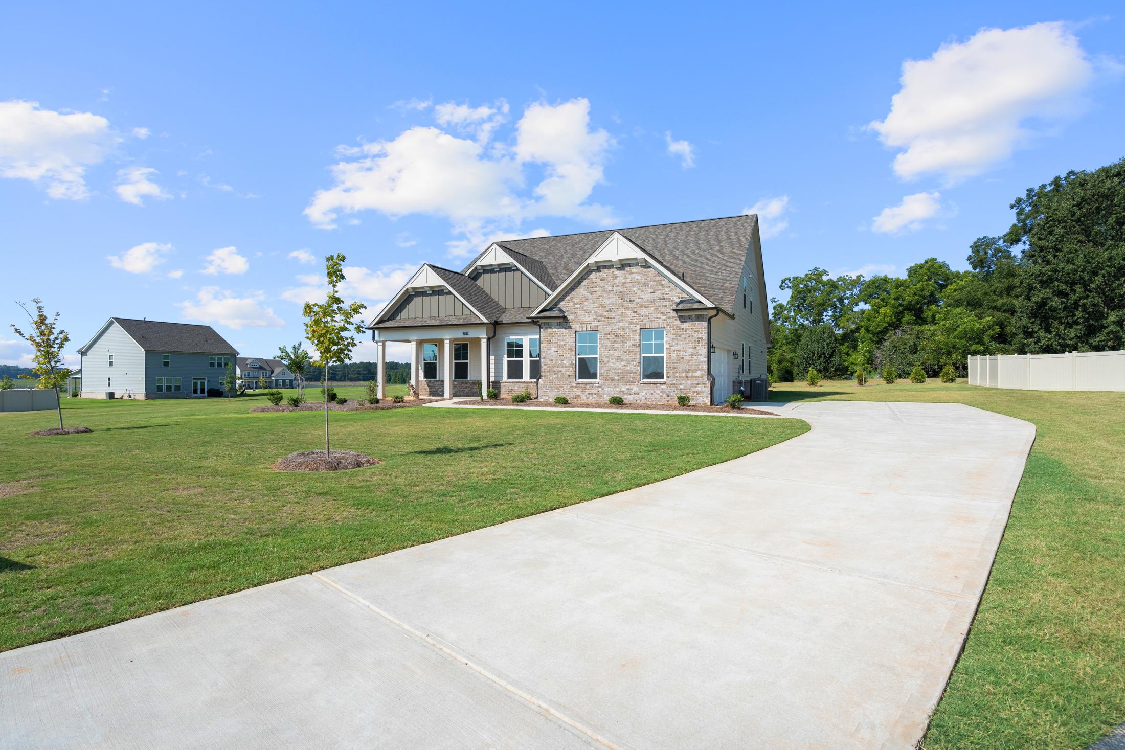 Two-story brick home exterior at Everleigh in Locust Grove GA with covered front porch, curved driveway, and green lawn